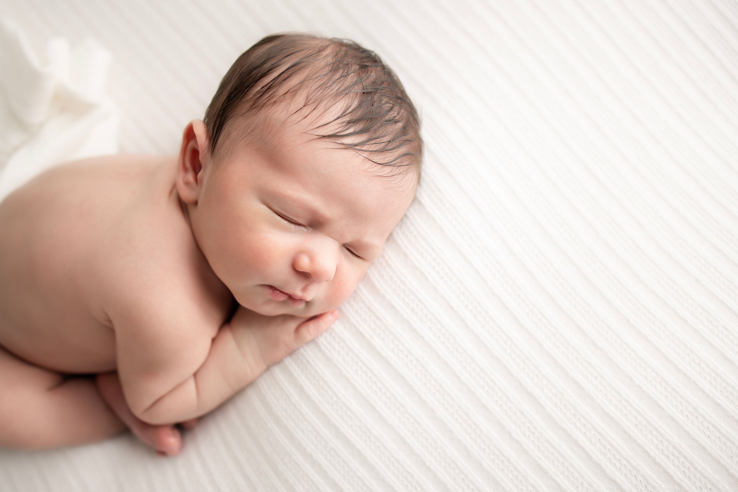 Peaceful sleeping newborn baby on soft white textured background.
