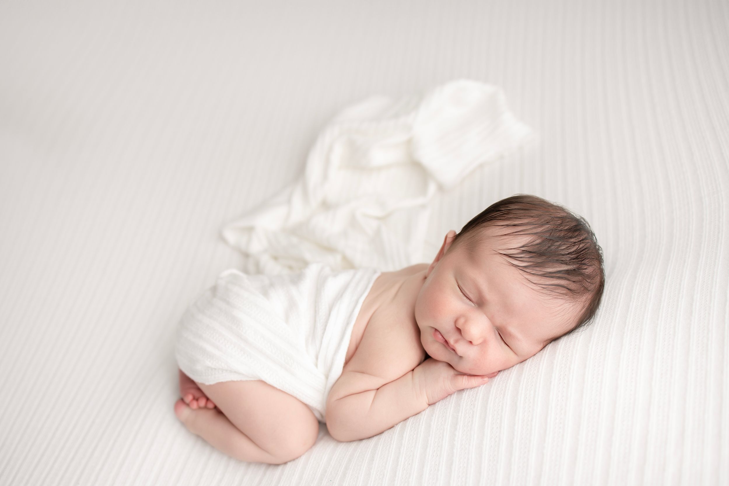 Newborn baby sleeping peacefully with white fabric wrap.