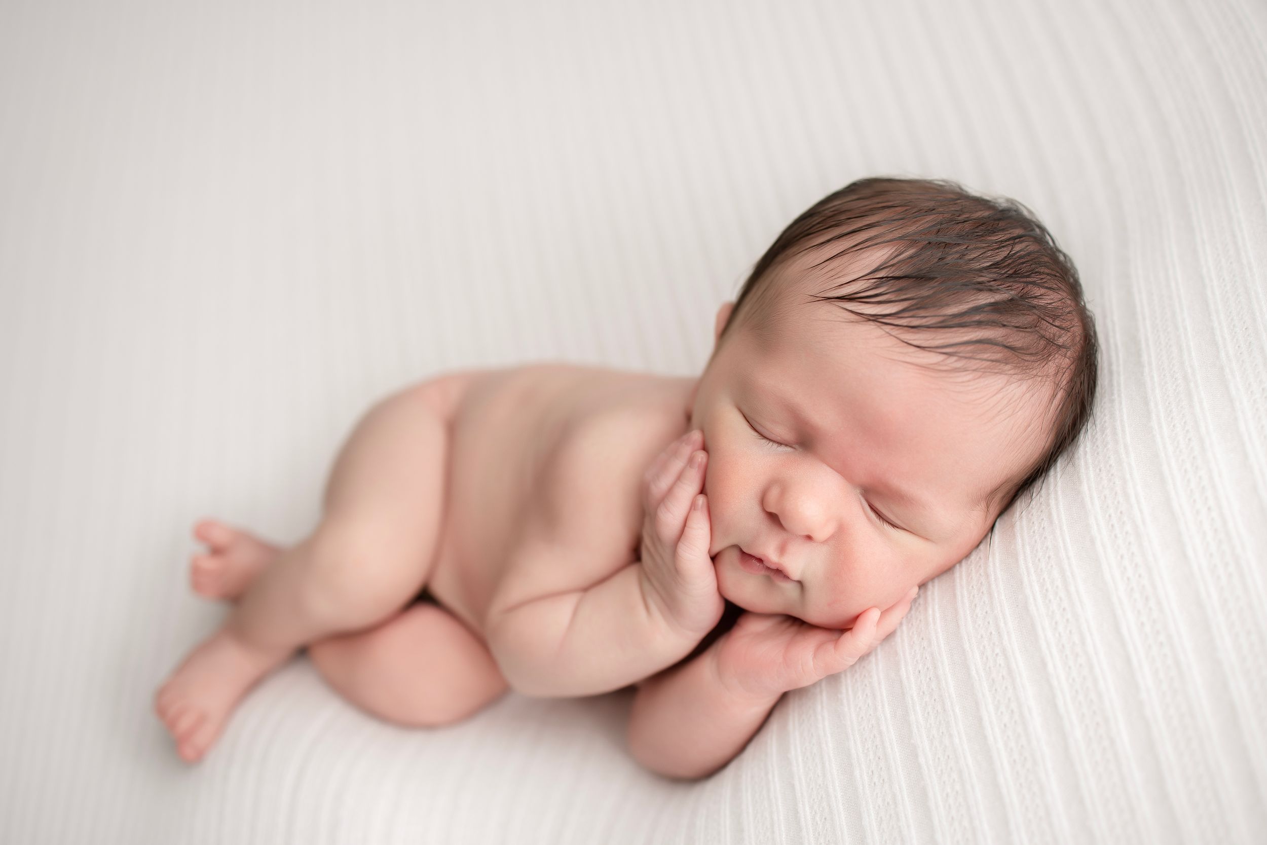 Sleeping newborn baby lying on side against white backdrop.