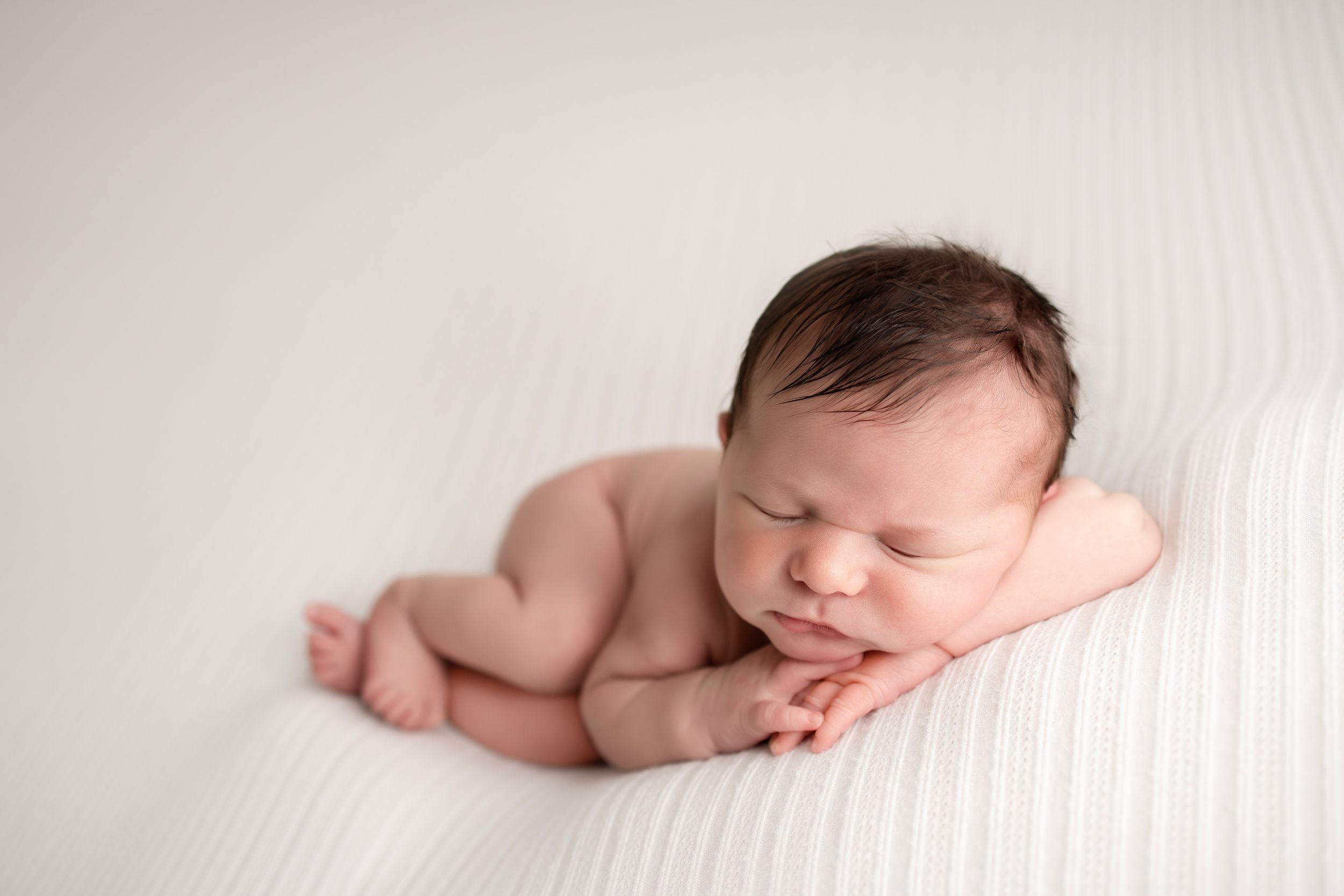 Newborn baby sleeping peacefully on white backdrop in natural pose.