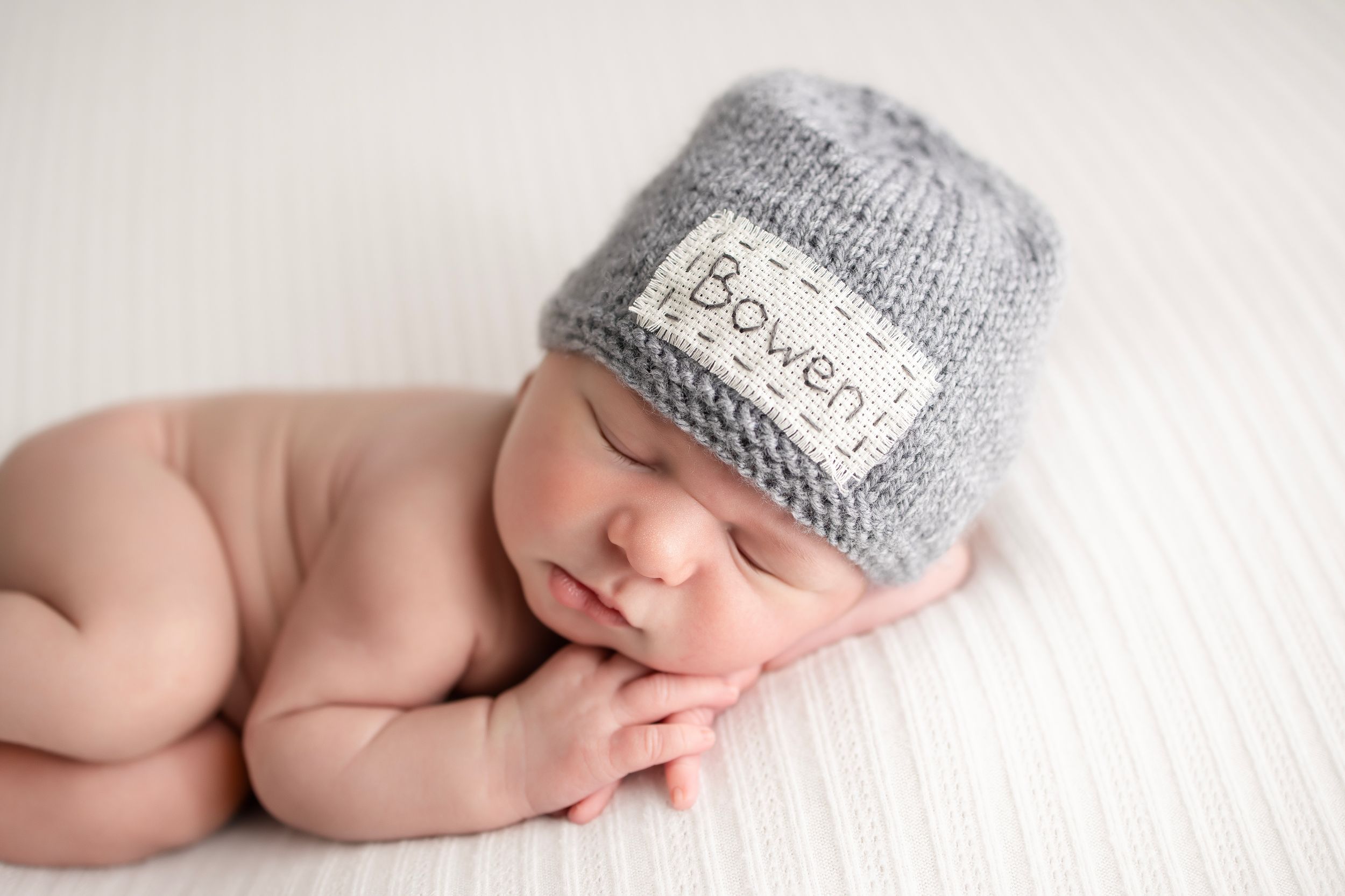 Sleeping newborn wearing gray knit hat on white background.