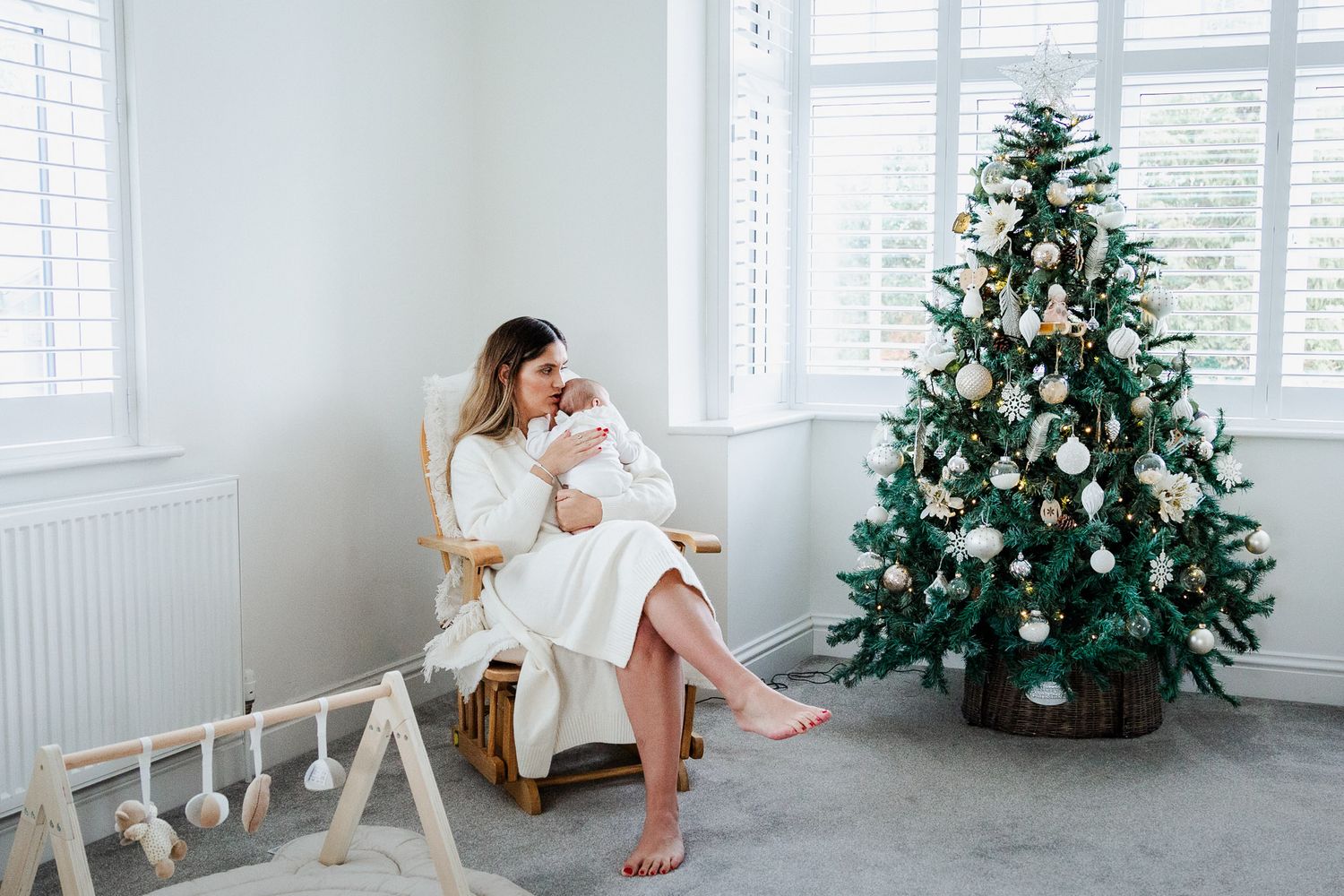 A mother and her baby sit in a chair by the Christmas tree. Bristol newborn photographer