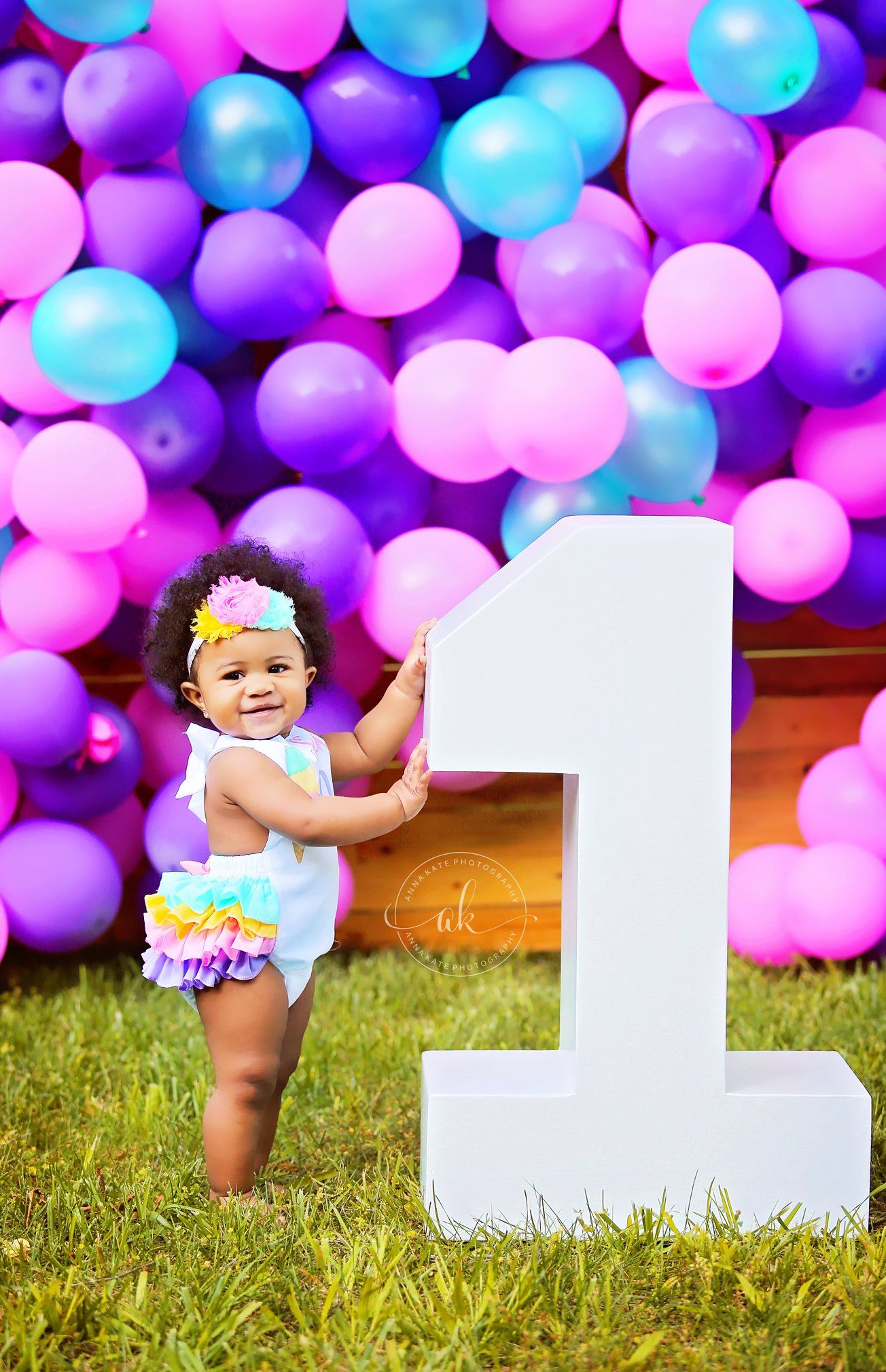 First birthday celebration setup with large white number one against purple and blue balloon backdrop.