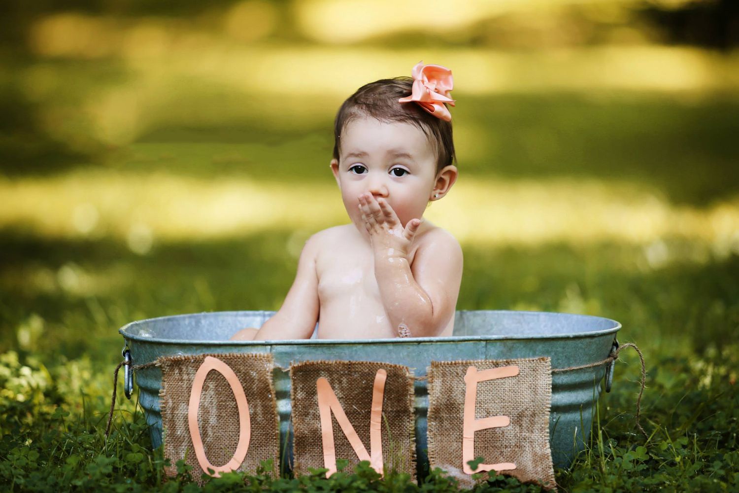 Baby sitting in rustic metal tub with 'ONE' letters displayed in outdoor setting.