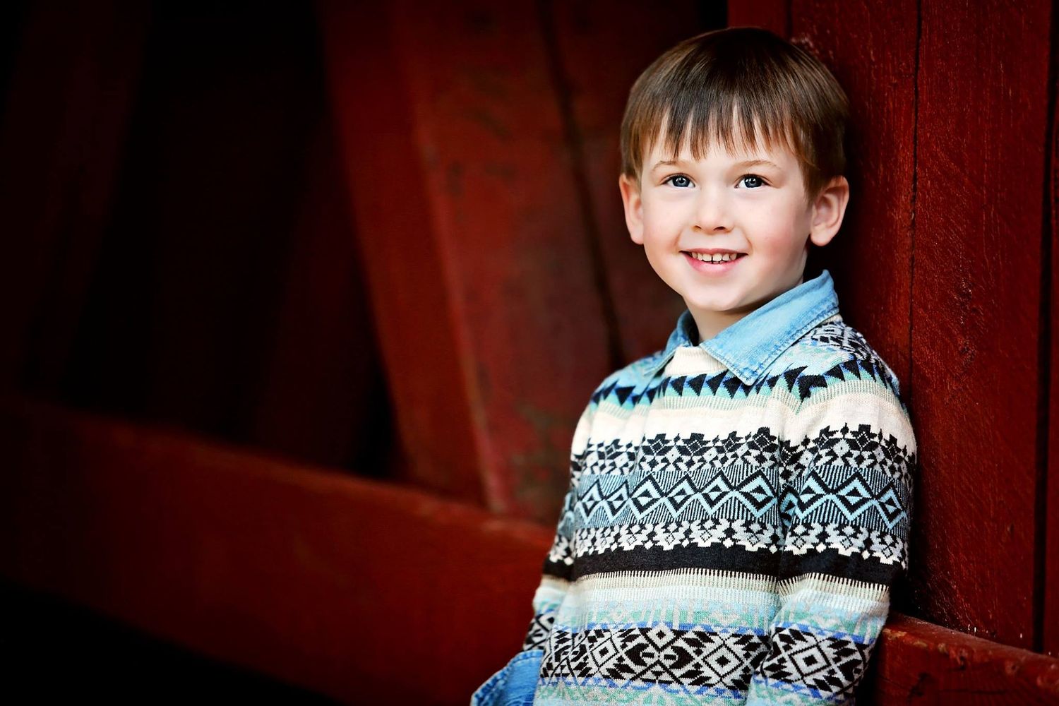 Portrait of child wearing fair isle sweater against red barn background.