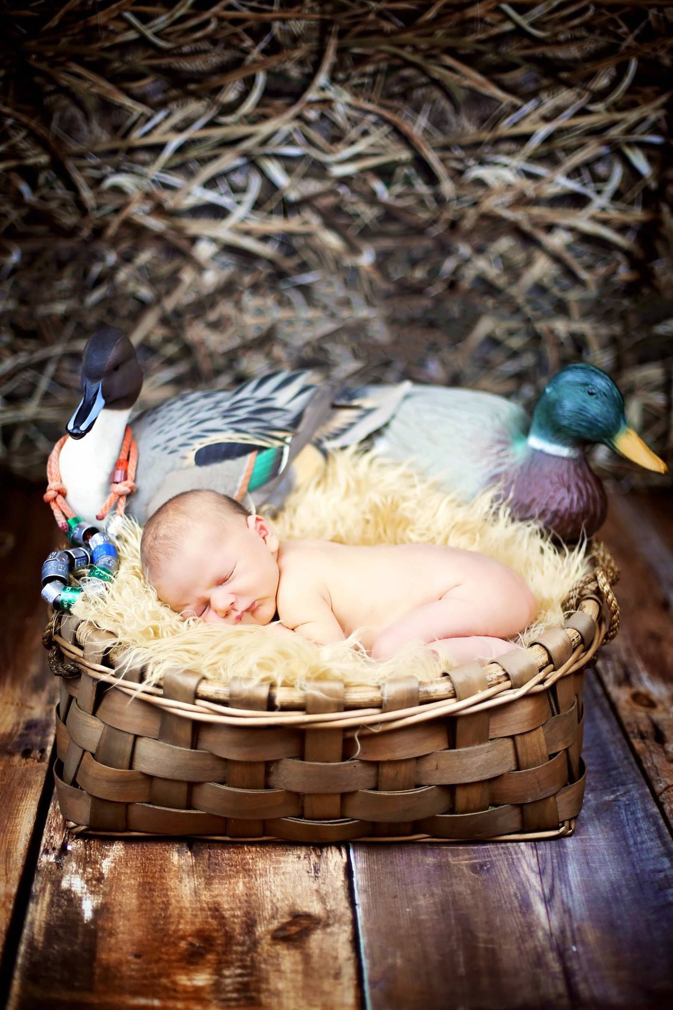 Sleeping newborn posed with decorative ducks in rustic woven basket on wooden surface.