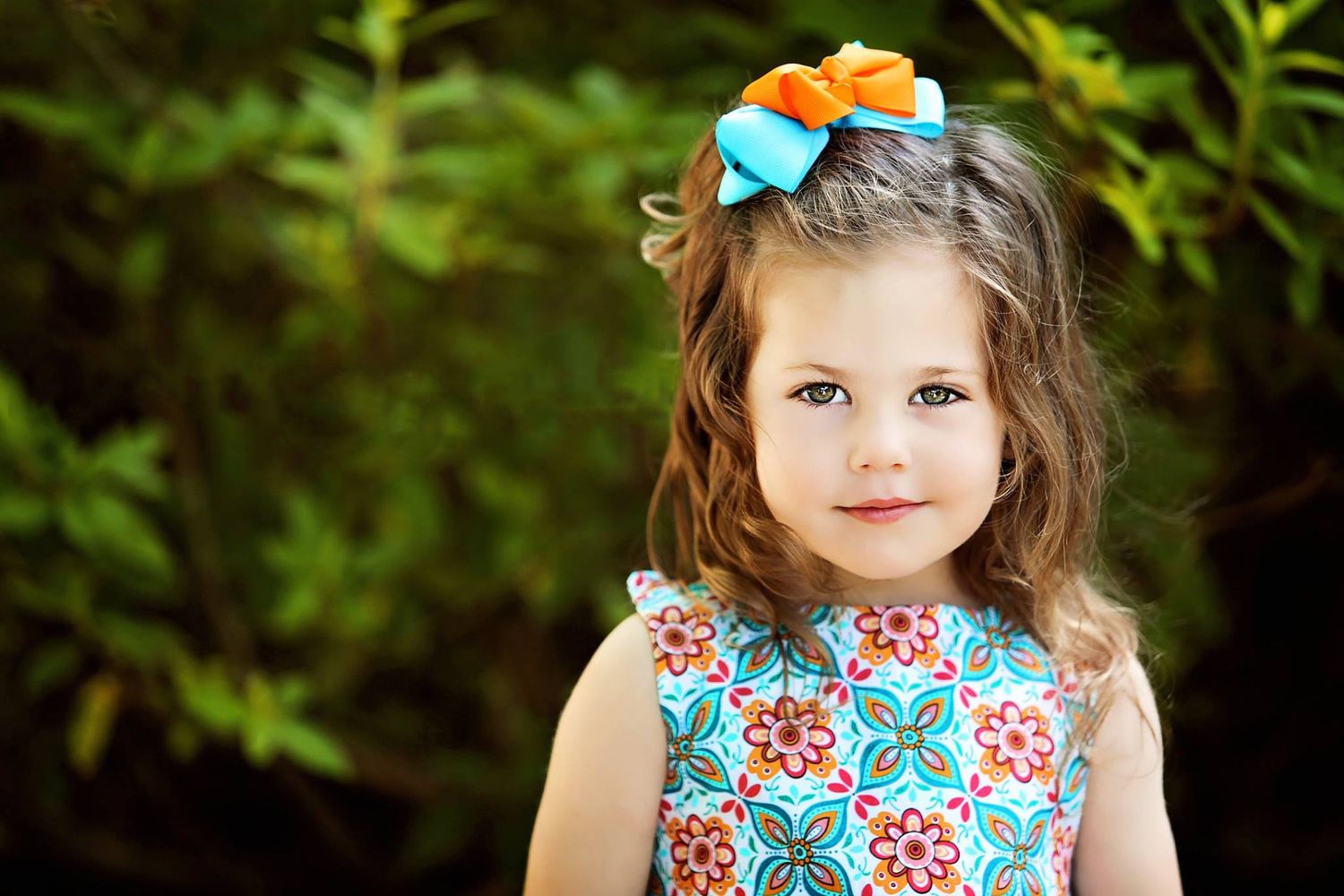 Young girl wearing floral print dress with blue bow outdoors.