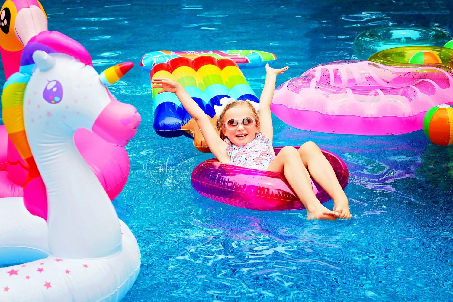 Summer pool scene with colorful inflatable floats including unicorn and donut shapes in bright blue water.