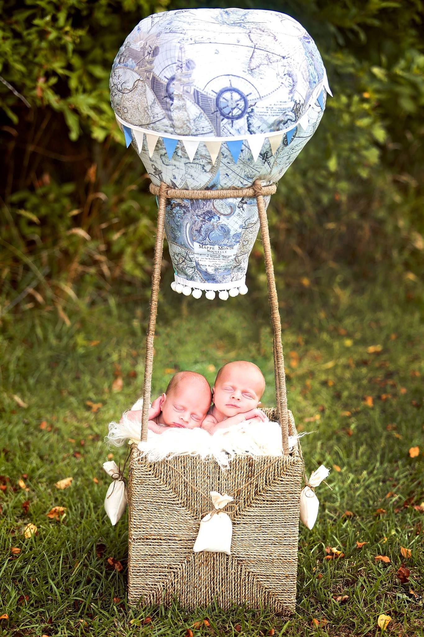 Sleeping newborns in decorative hot air balloon prop outdoors.