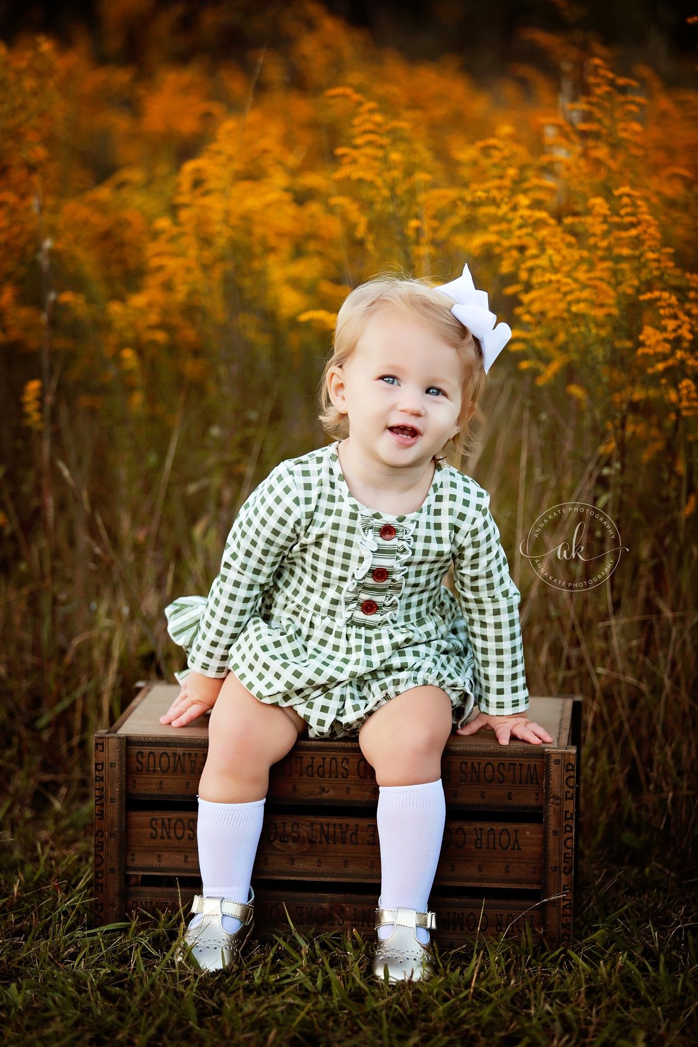 Fall portrait of a small child sitting on a wooden crate surrounded by golden autumn foliage.