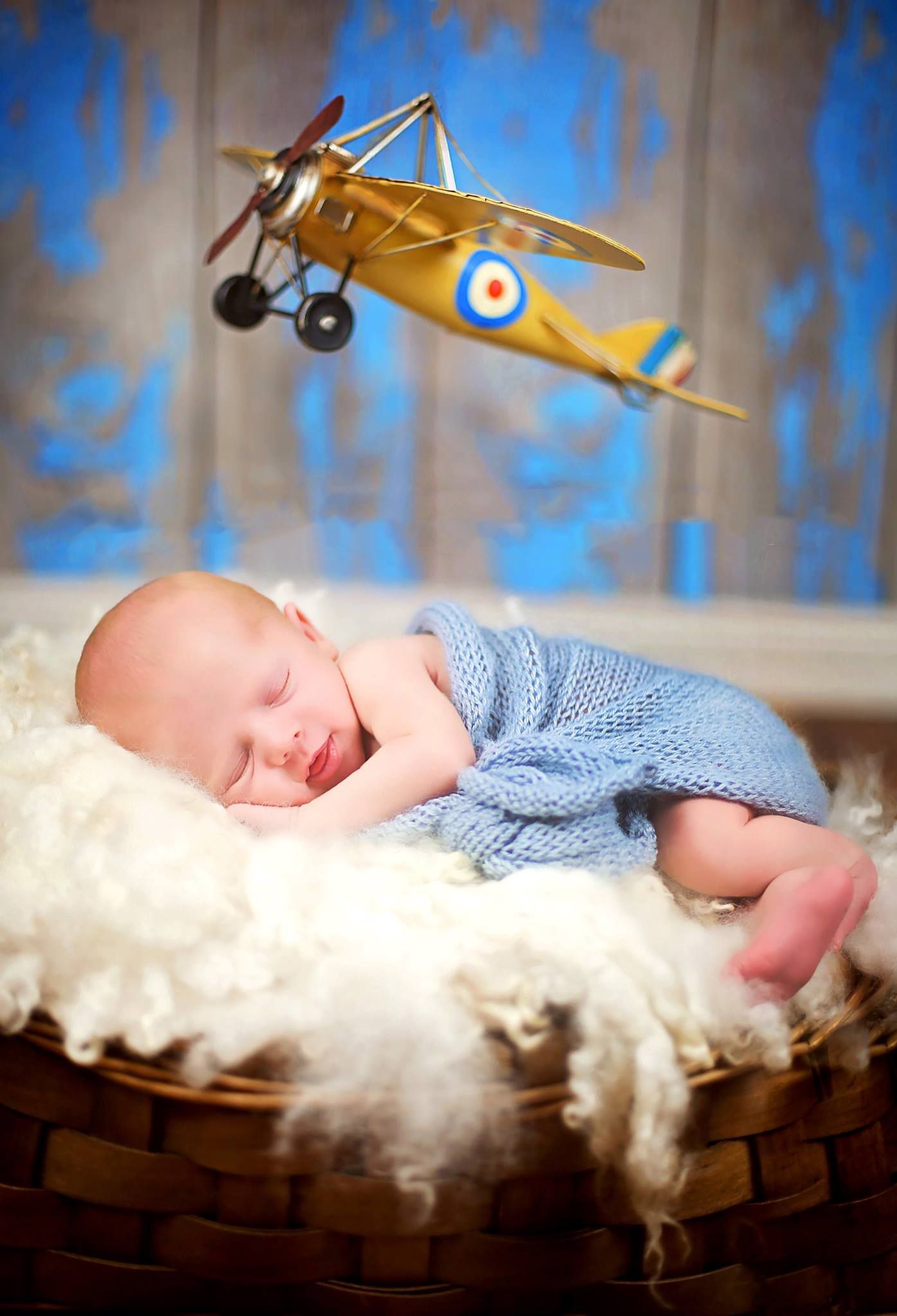Sleeping baby in blue wrap with vintage yellow airplane prop floating above.