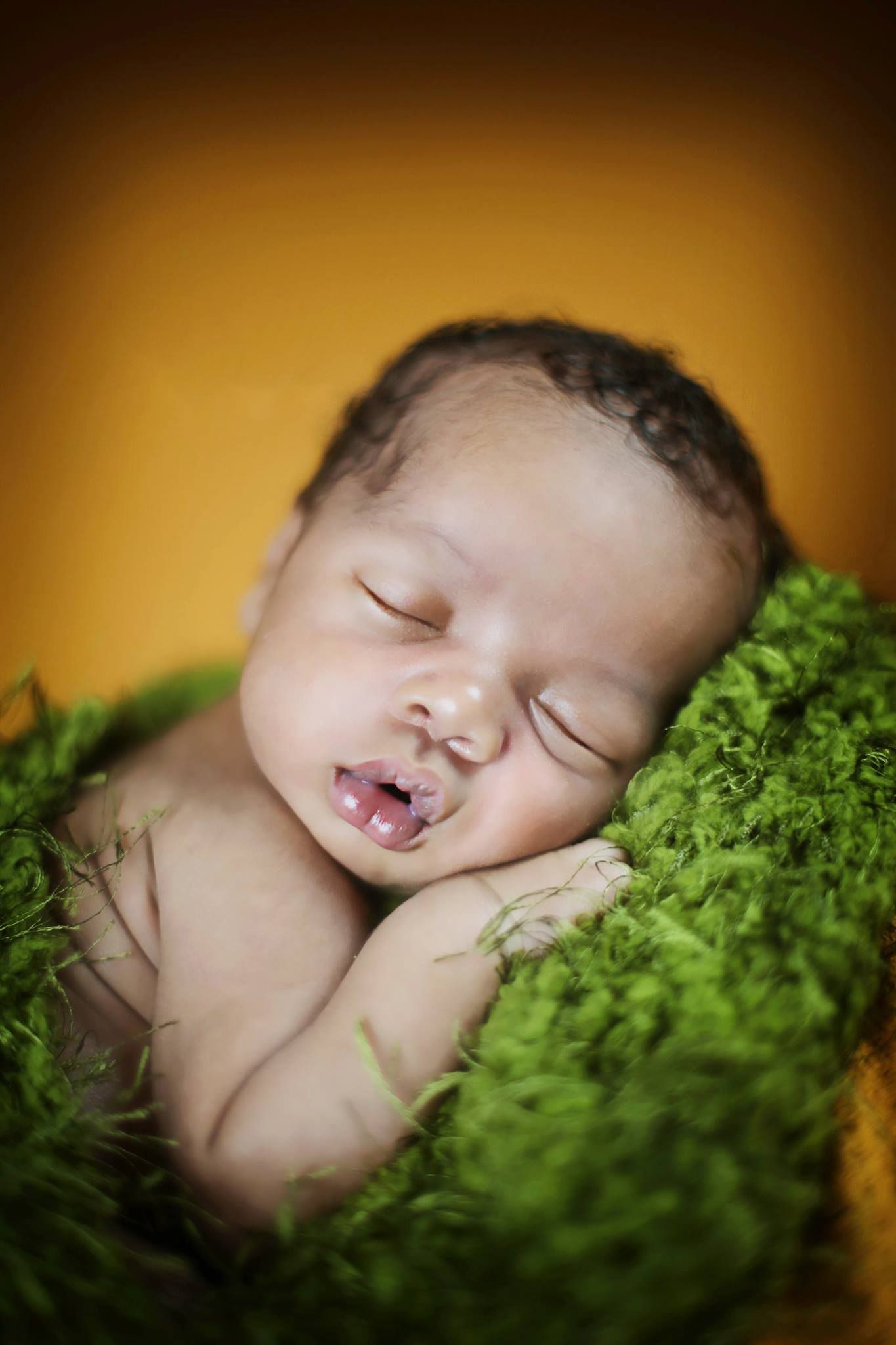 Peaceful sleeping newborn nestled in soft green moss with warm amber background lighting.