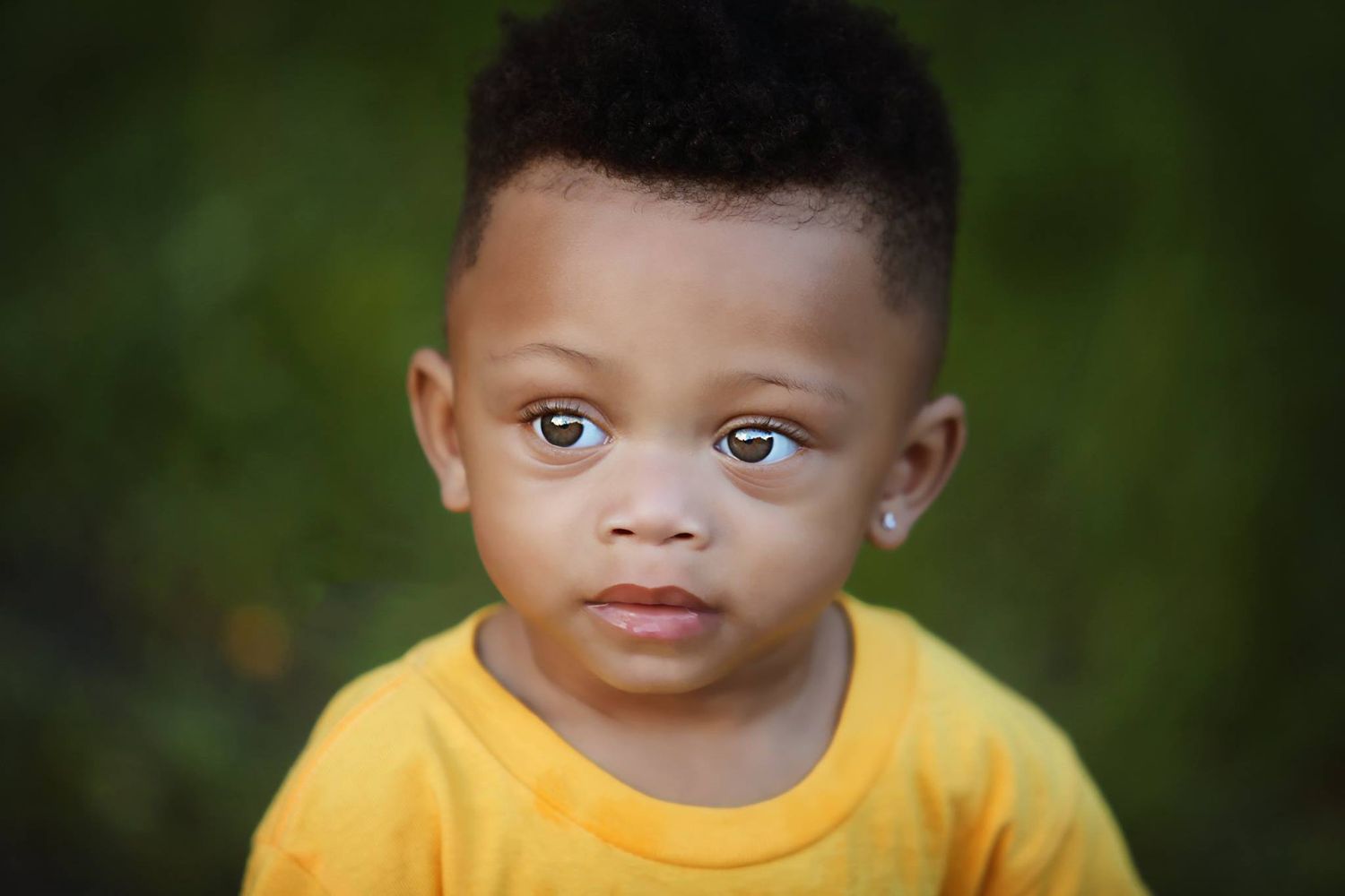 Close up portrait of young child in yellow t-shirt against green background.