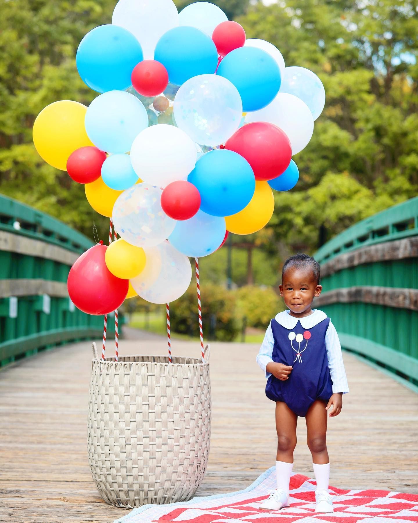 Colorful balloons tied to a white basket on a wooden bridge featuring festive red, blue, yellow and white colors.