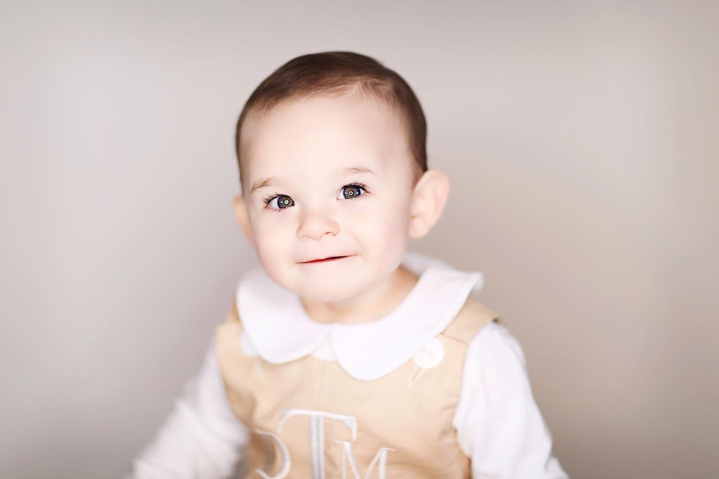 Baby in tan and white collared outfit smiling at camera.