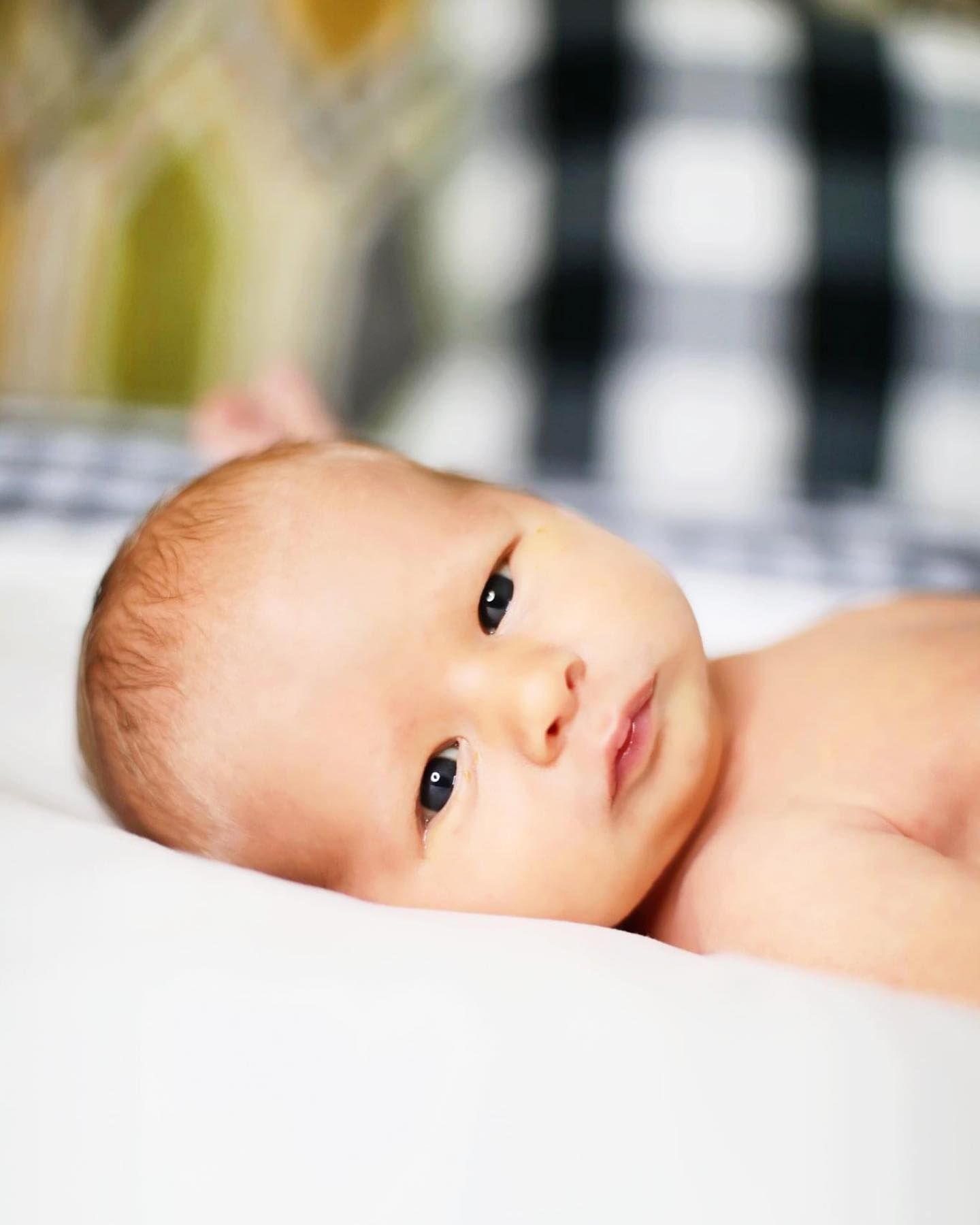 Close up portrait of infant lying on checkered blanket.
