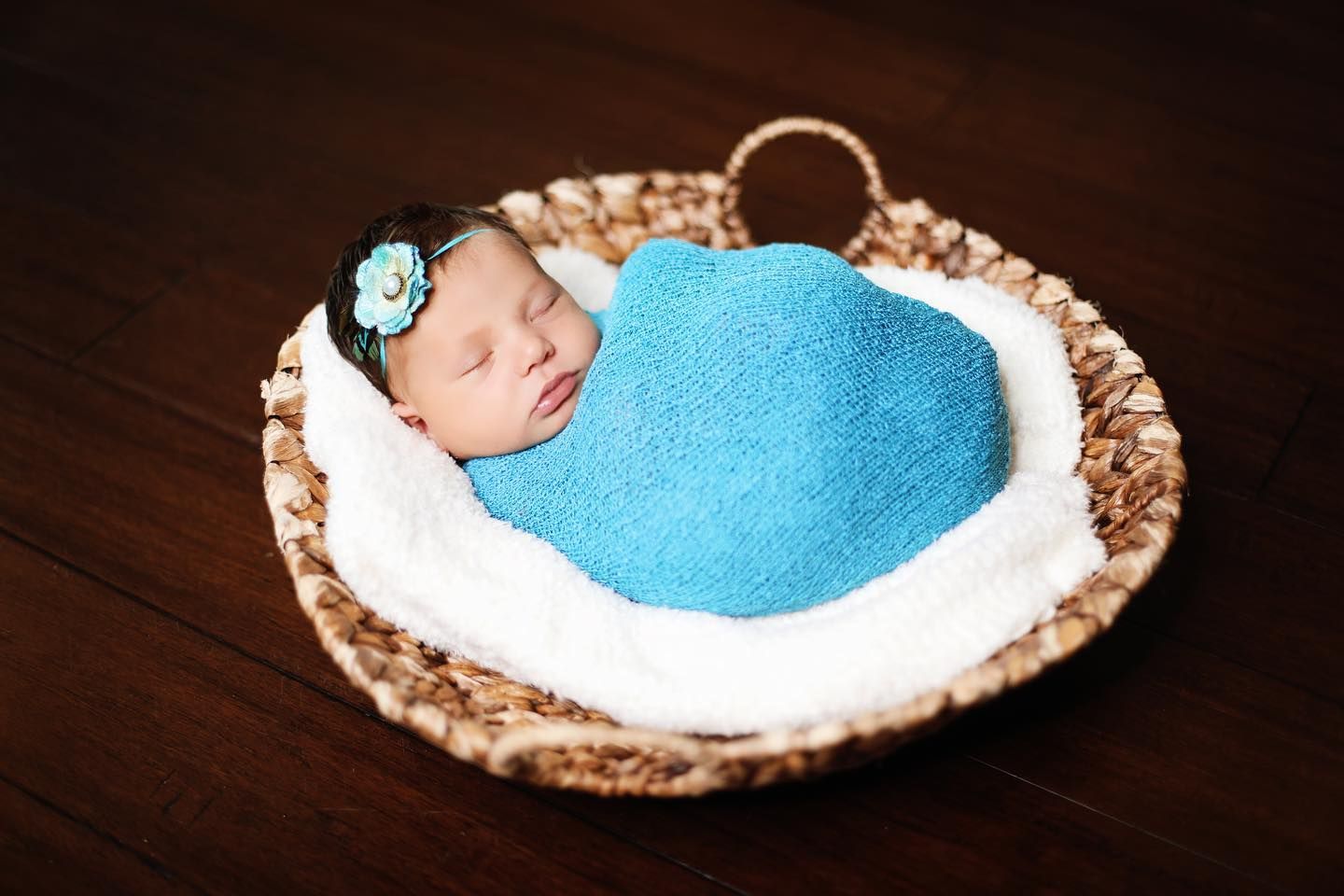 Sleeping newborn wrapped in blue blanket in textured basket.