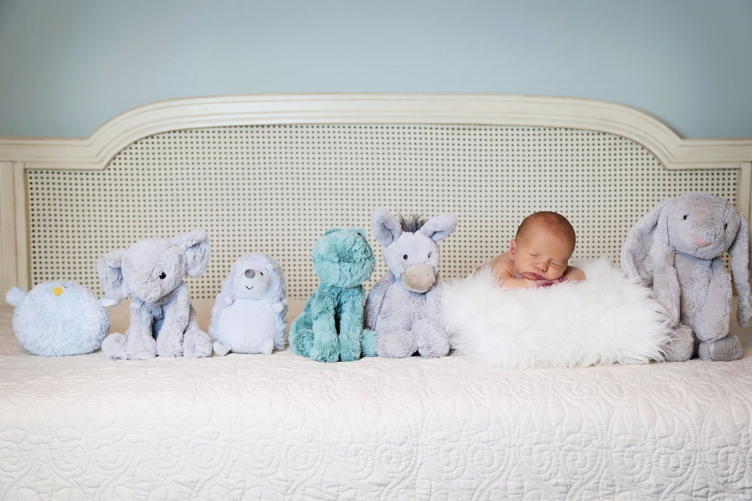 A sleeping baby surrounded by soft plush animal toys on a white bed.