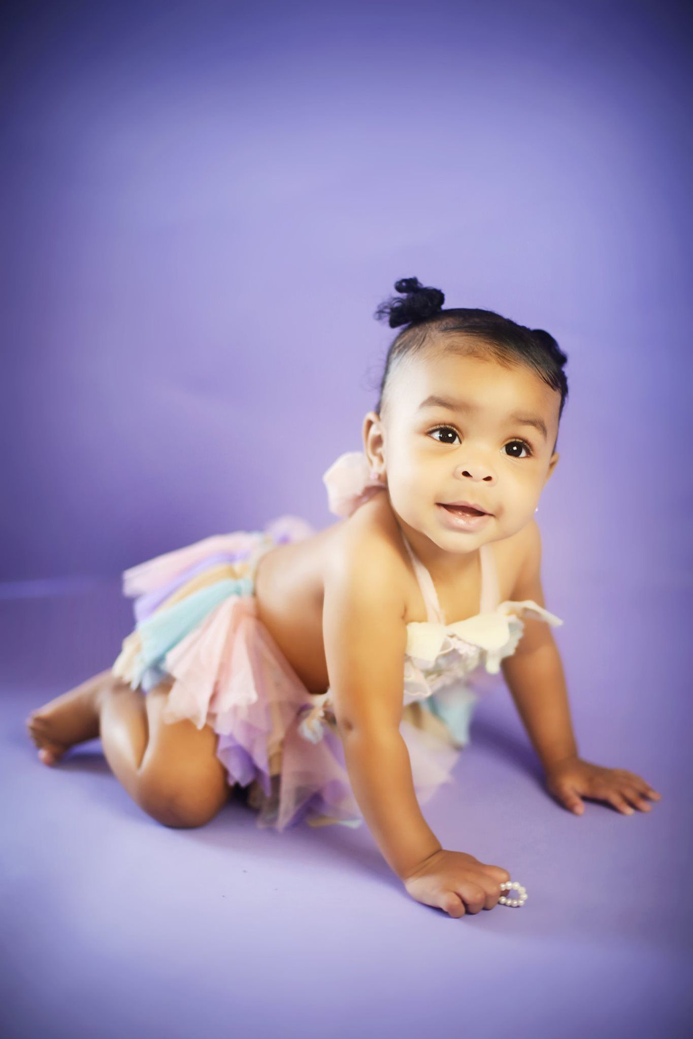 Baby in pastel tutu photographed against purple backdrop during studio photoshoot.