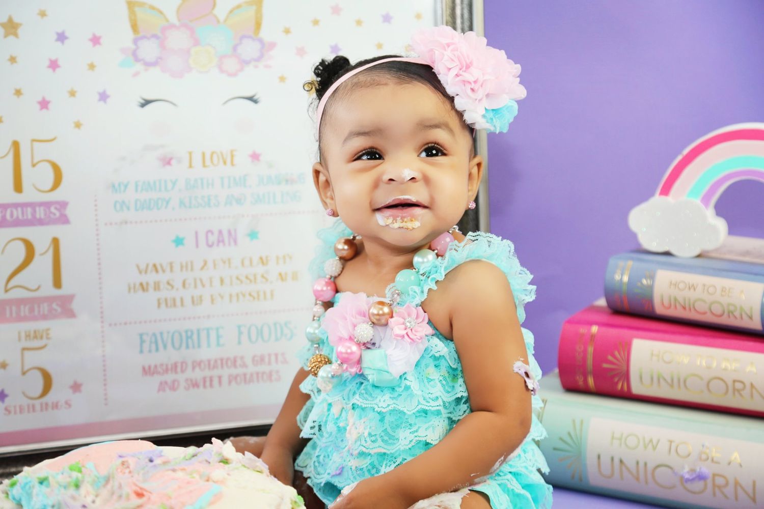 Unicorn themed first birthday setup with decorative rainbow backdrop and stacked books.