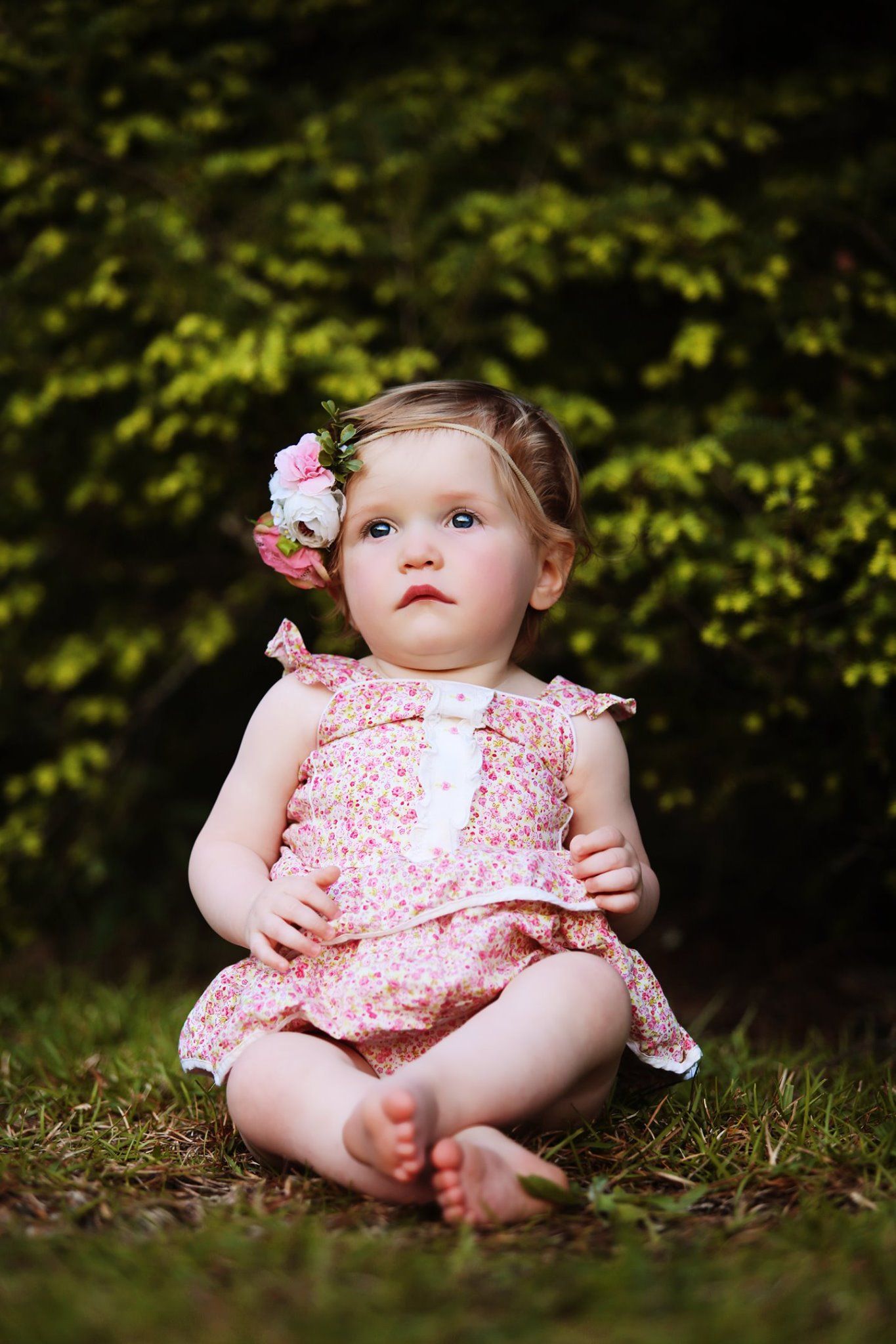 Outdoor portrait in pink floral outfit with flower hair accessory against green foliage background.