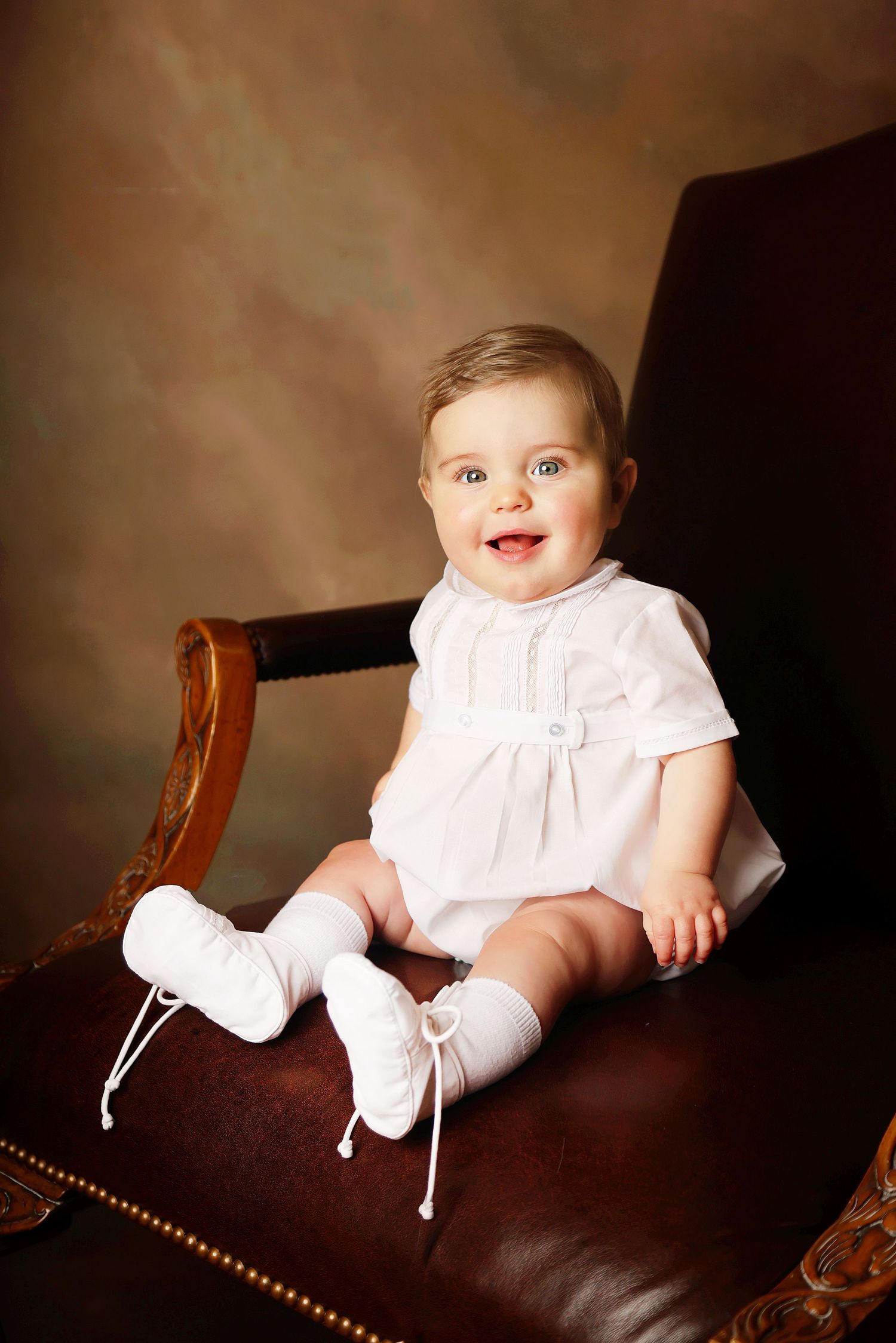 A baby in a white dress sits atop a brown leather sofa in a series of progressive poses from side to front view.