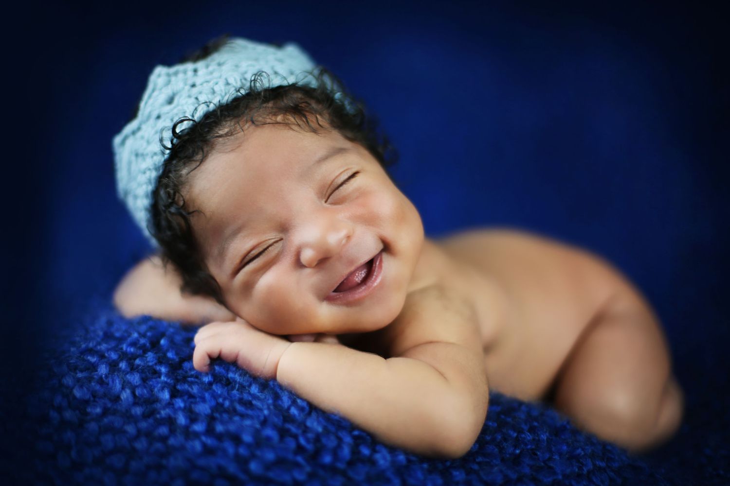 Newborn with lace headband sleeping on blue knitted blanket.