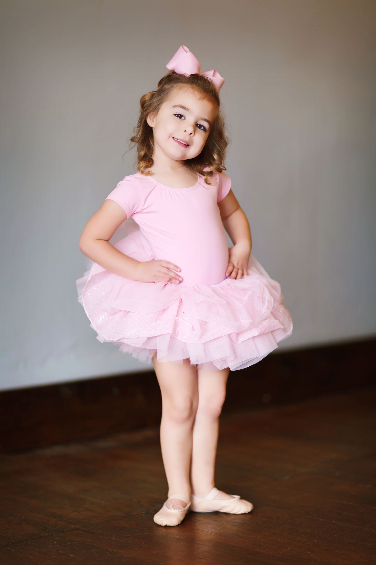 Young ballerina in pink tutu dress posing gracefully on wooden floor.