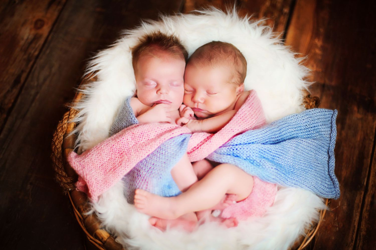 Sleeping newborn twins wrapped in pink and blue blankets on white fur.