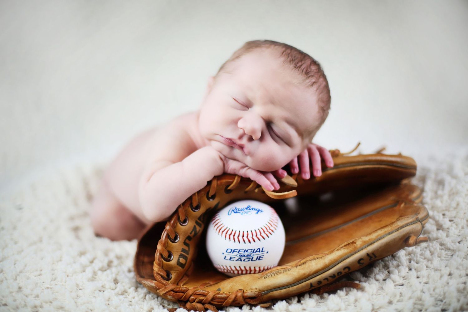 Newborn baby sleeping peacefully in baseball glove with baseball during studio portrait.