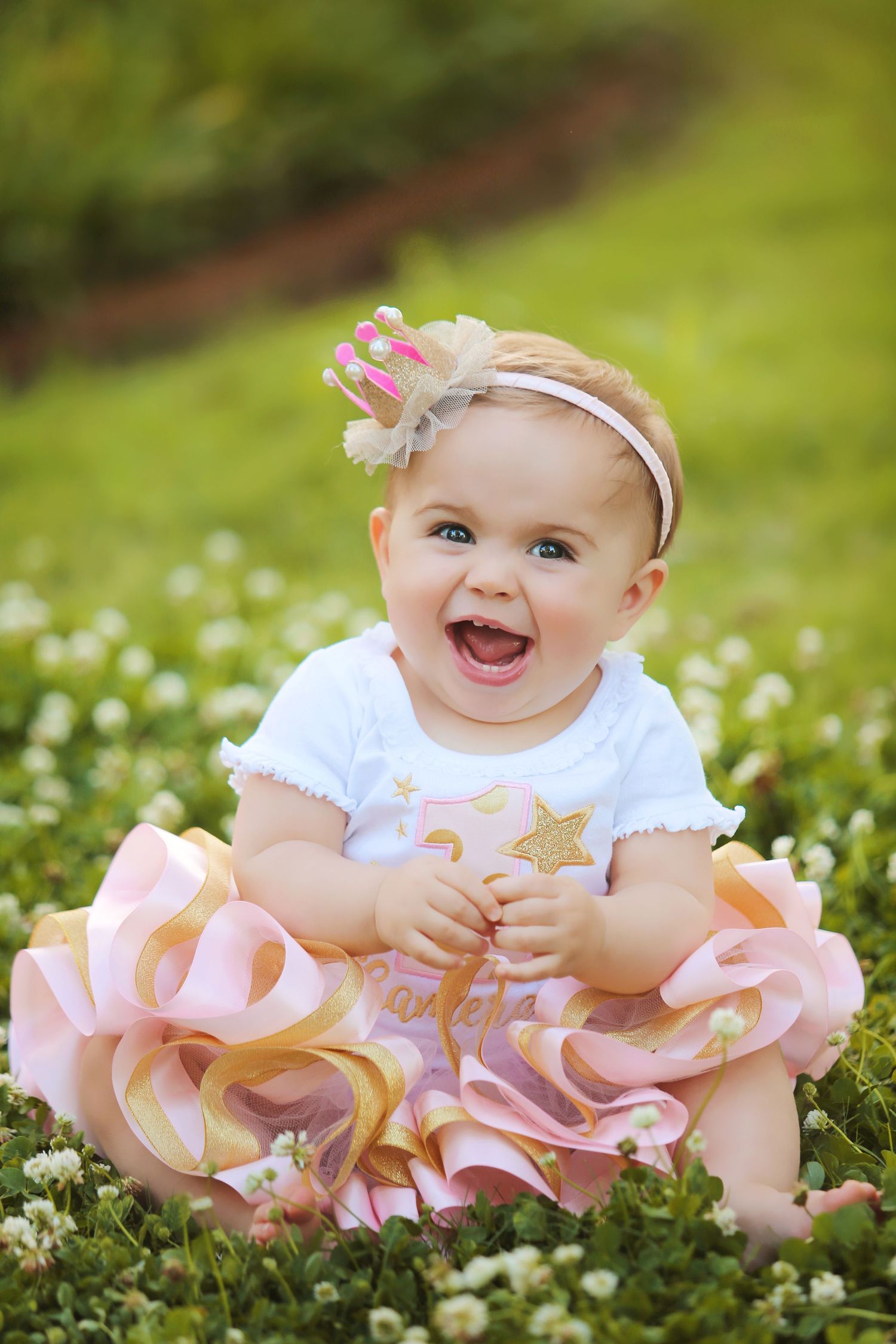 Baby wearing pink tutu dress sitting in field of white flowers during spring outdoor photoshoot.