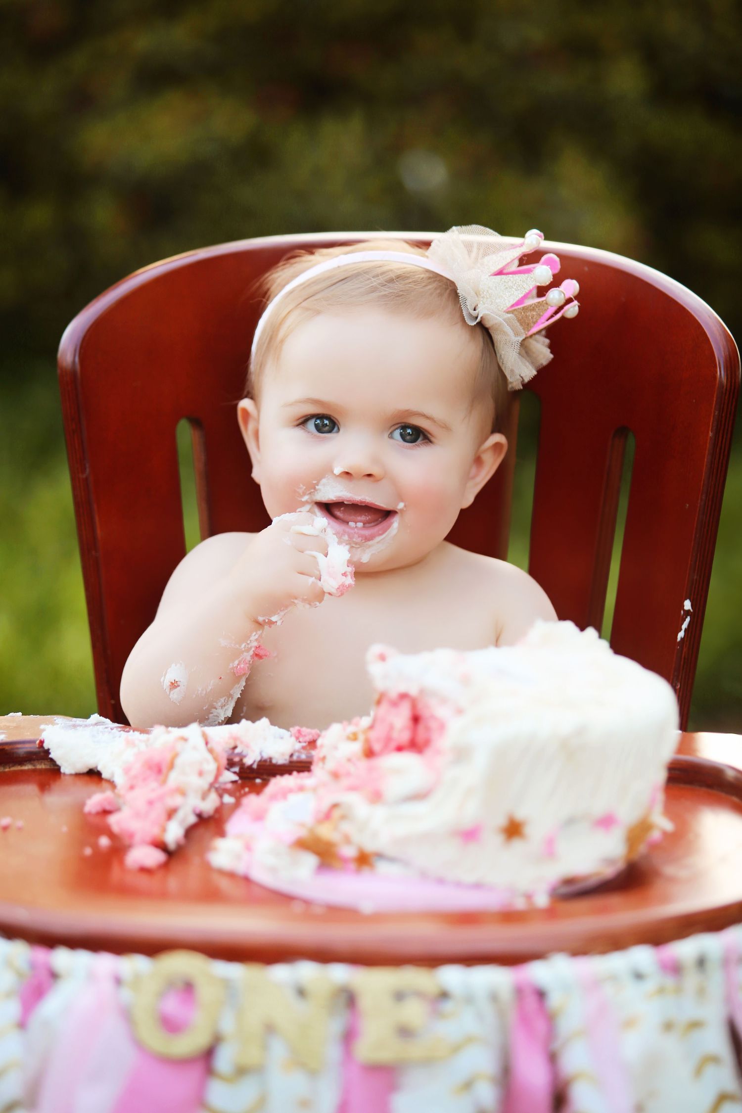 Baby enjoying first birthday cake smash photoshoot on red vintage chair outdoors.