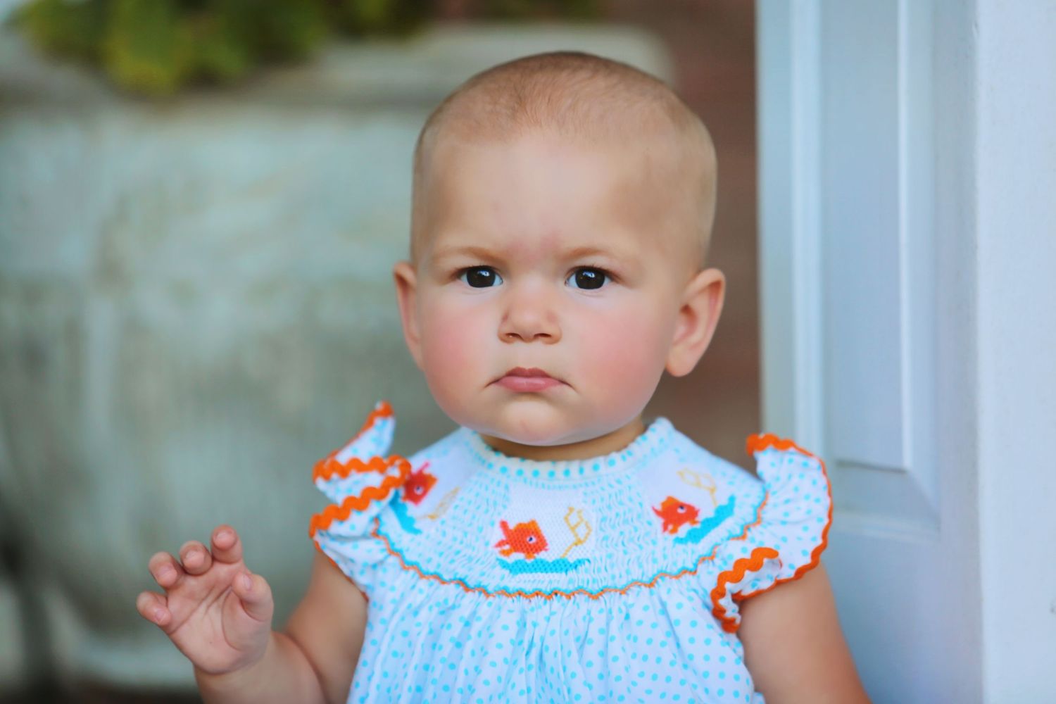 Baby in blue floral dress looks at camera.