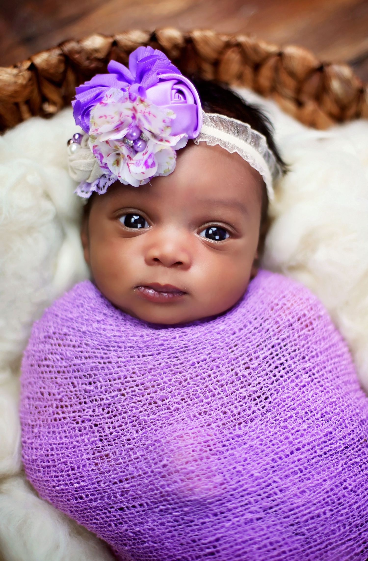 Newborn wrapped in purple swaddle wearing floral headband during studio portrait session.