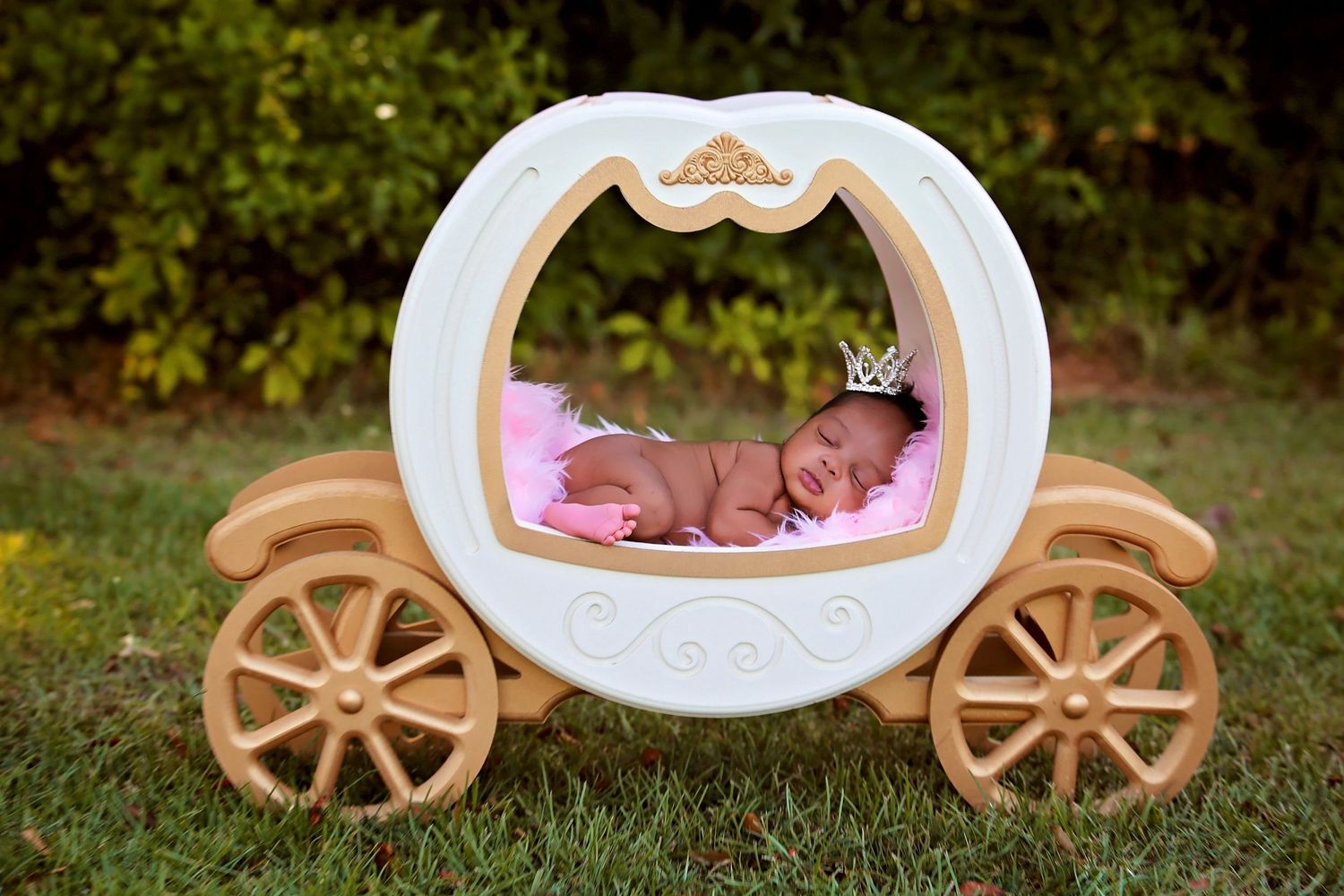 Newborn baby sleeping in decorative white carriage prop during professional photo session.