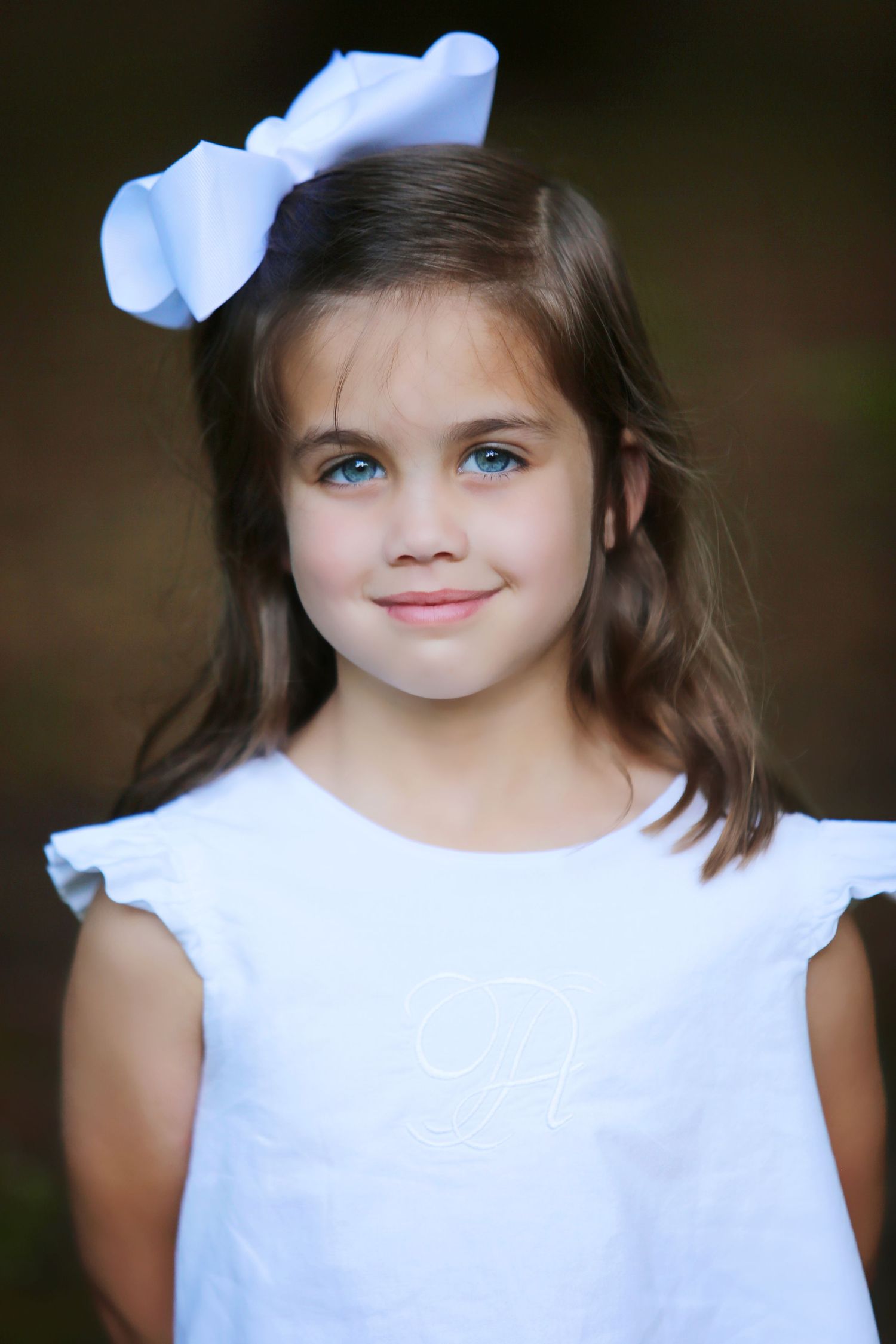 Young child in white dress with blue bow smiling at camera.