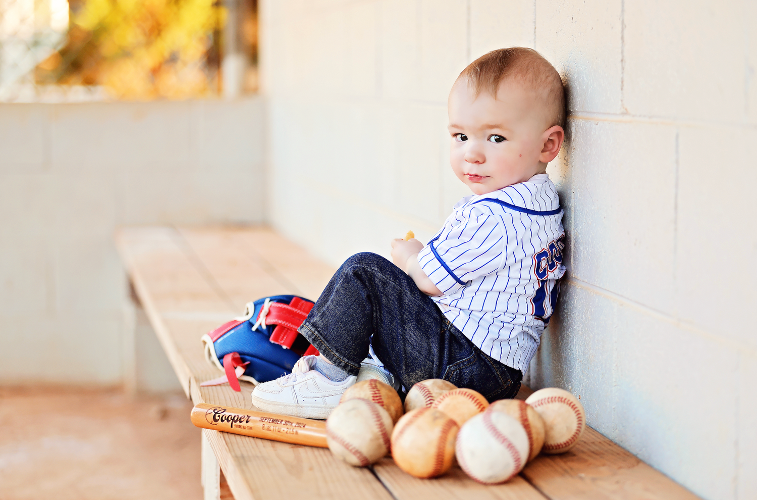 A baby in blue and white stripes lies on a cozy wooden floor near soft plush toys and blankets.