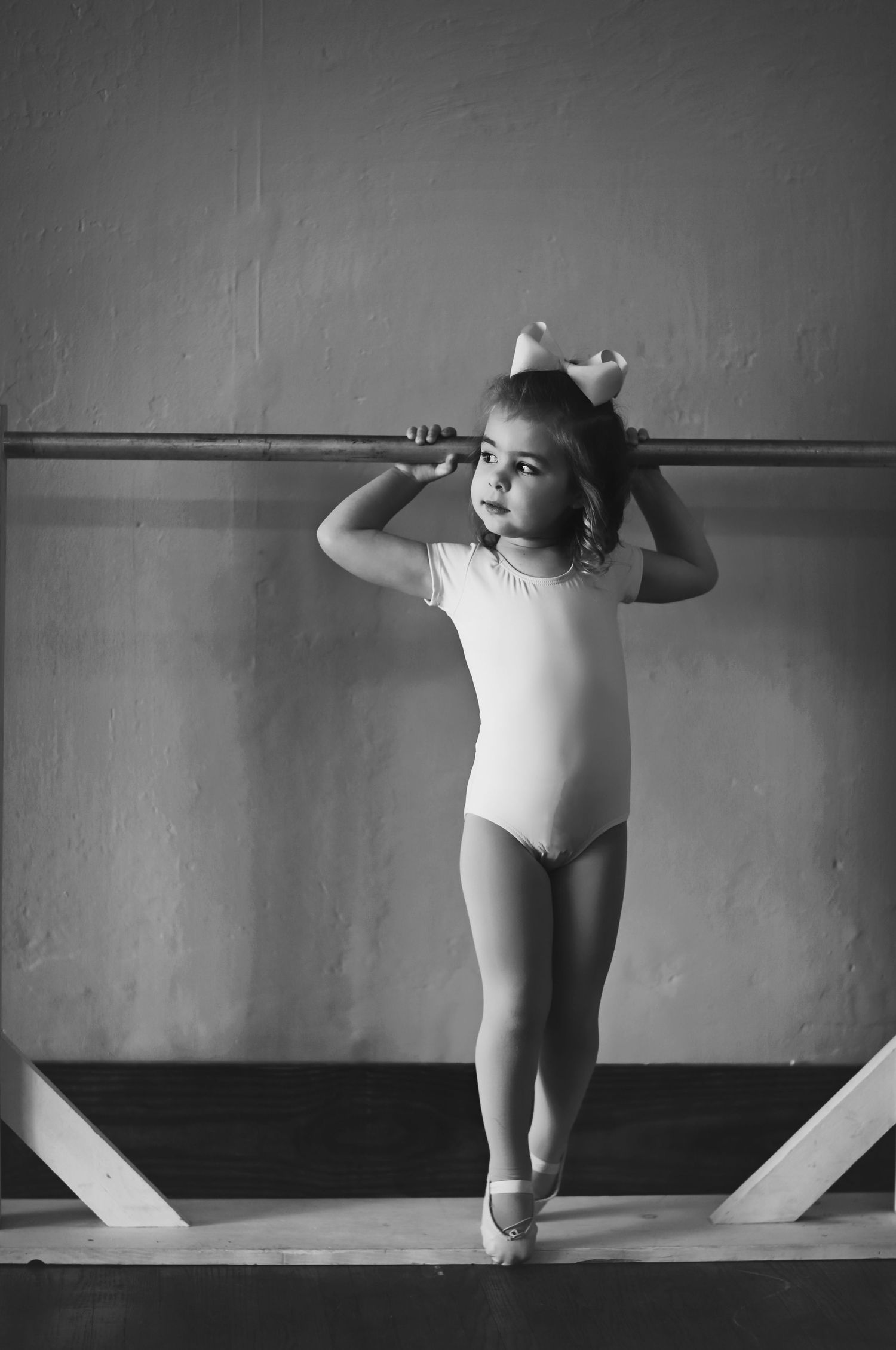 Ballet dancer practicing at barre in black and white photography.