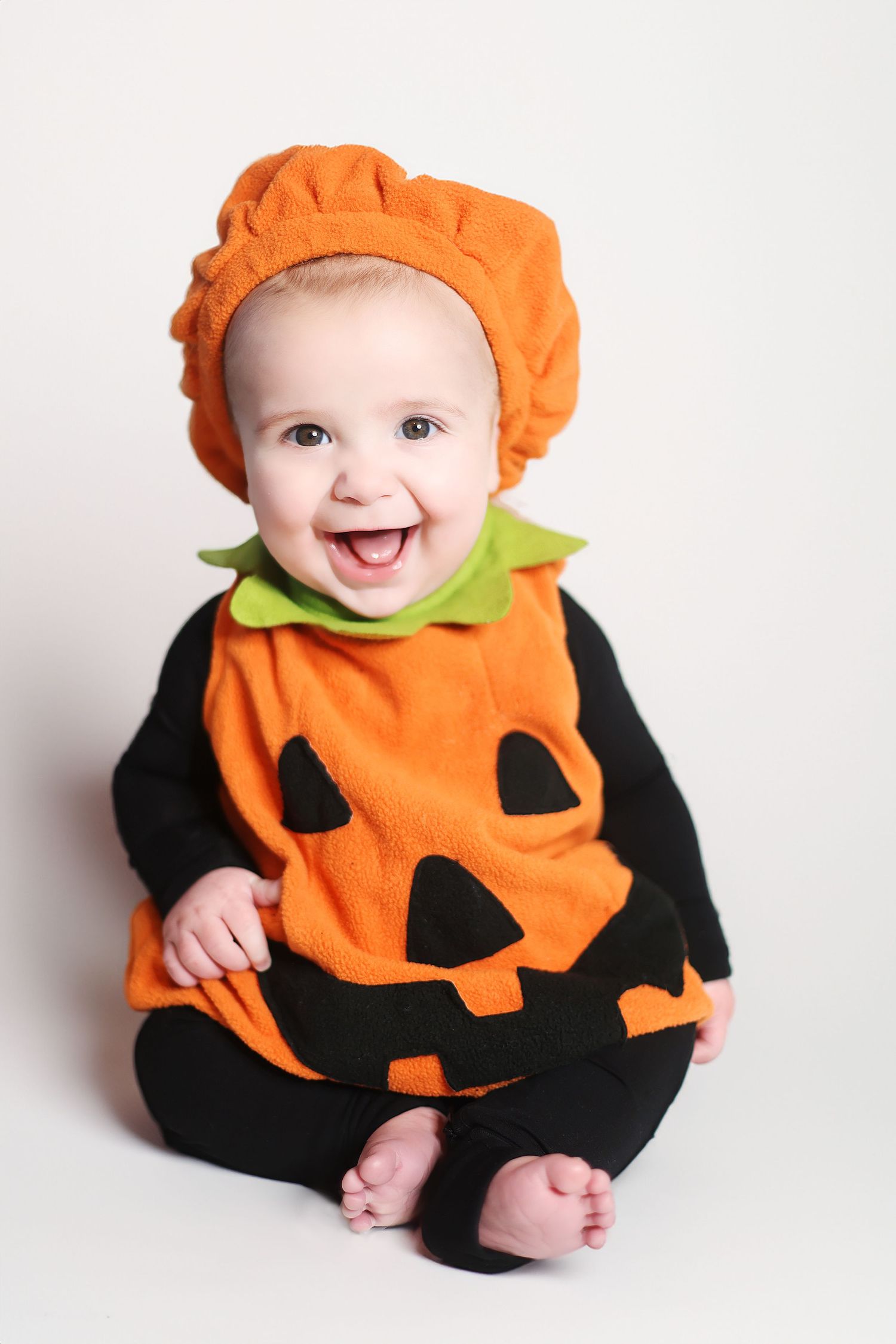 Baby wearing an adorable orange pumpkin costume smiles at the camera.
