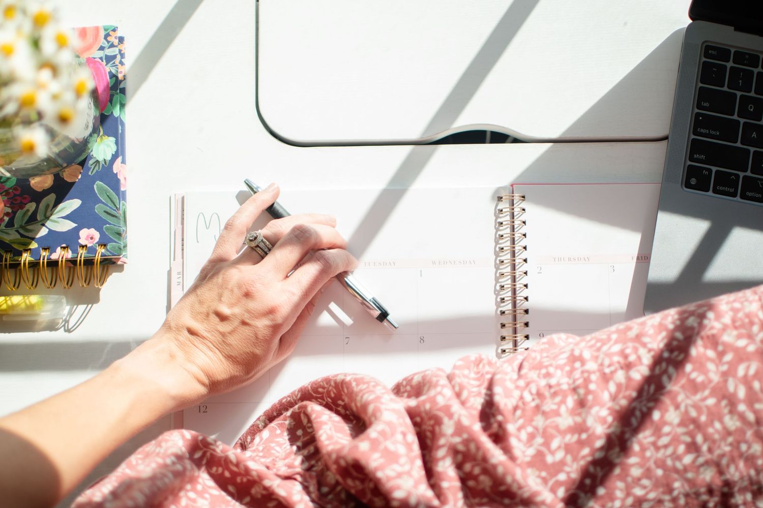 Hands typing on laptop keyboard with pink fabric and natural sunlight casting shadows.