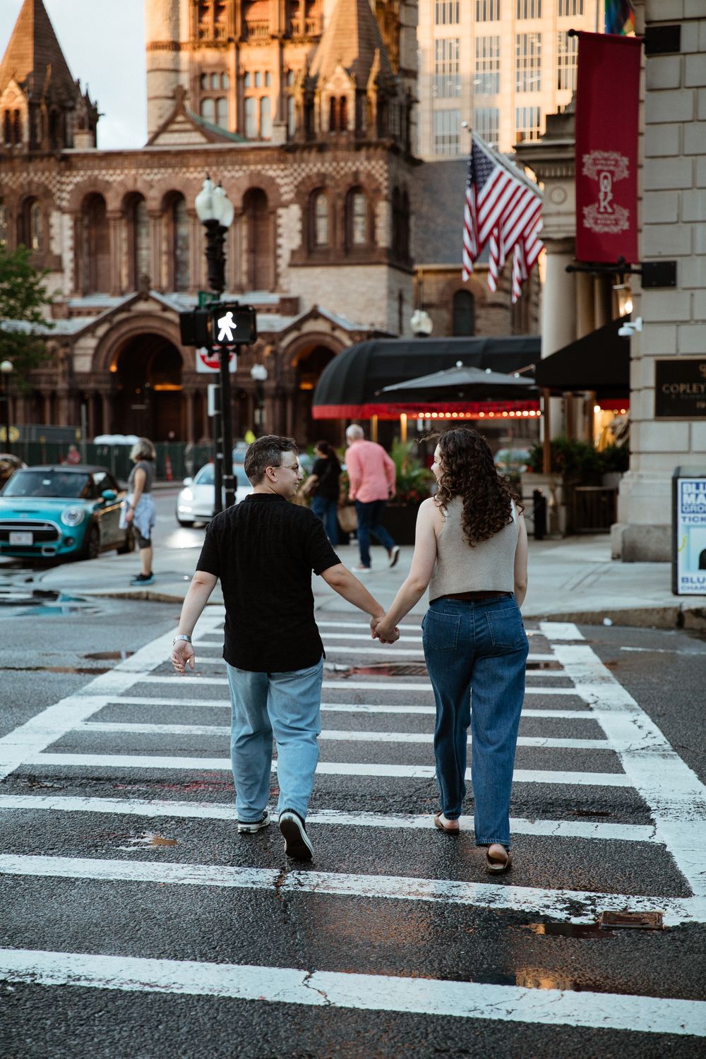 Couple walking across a crosswalk holding hands with historic buildings in the background.