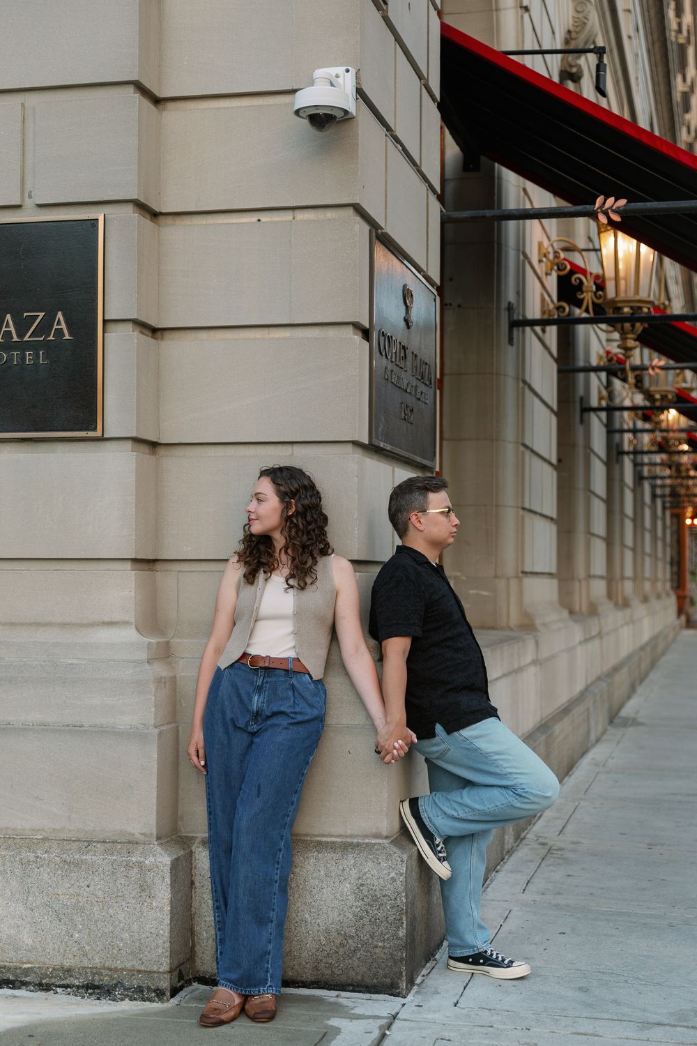 Playful couple posing and interacting along a building wall in an urban setting.