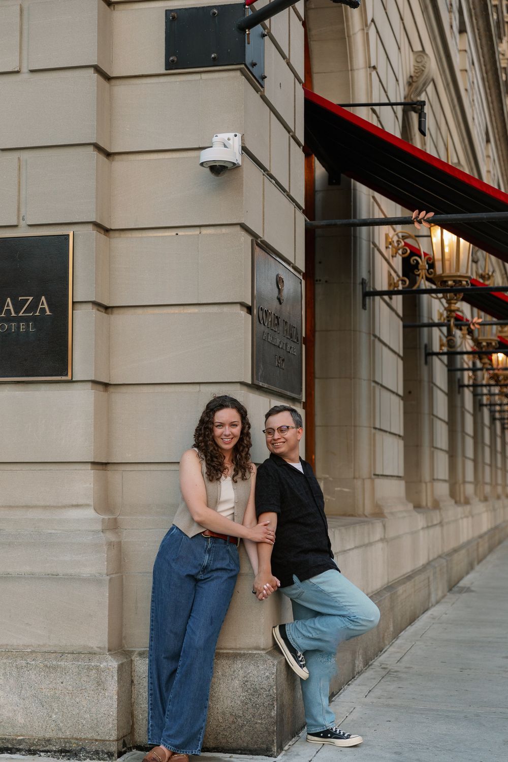 Romantic couple shares playful moments against a beige stone building wall.