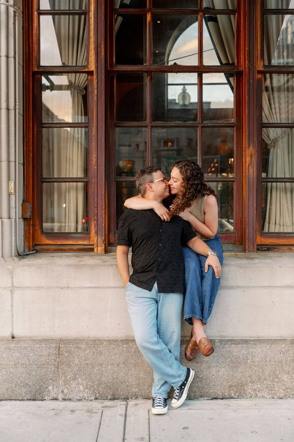 Couple shares intimate moments by large windows of a historic building.
