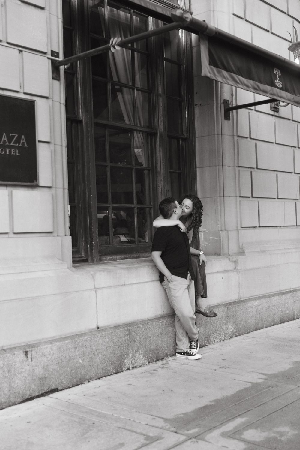 Couple embraces against stone architecture in black and white photography.