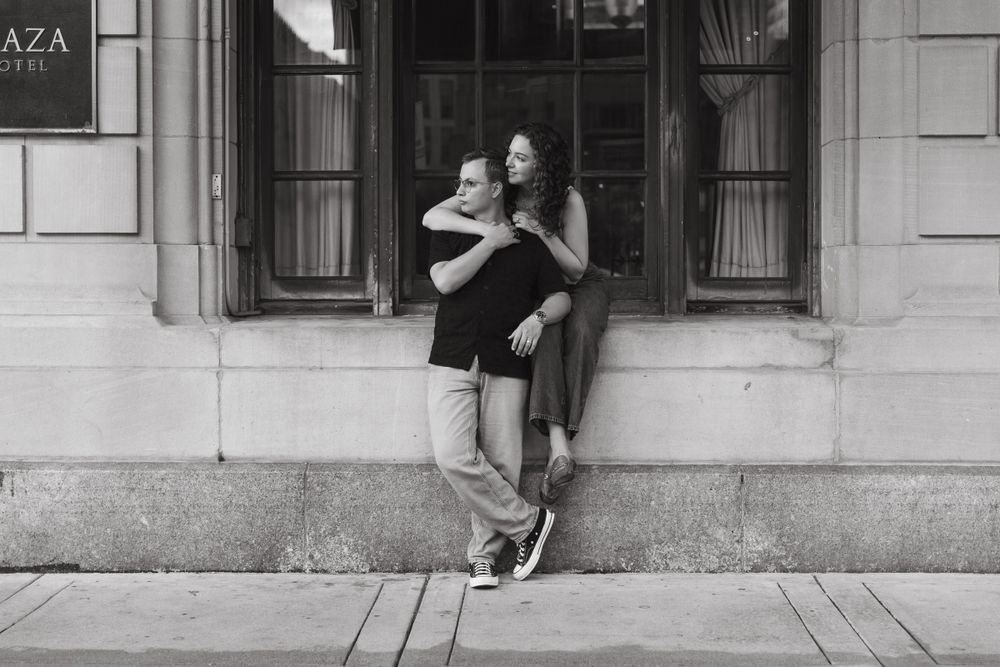 Couple poses playfully against urban architecture with wooden window frames.