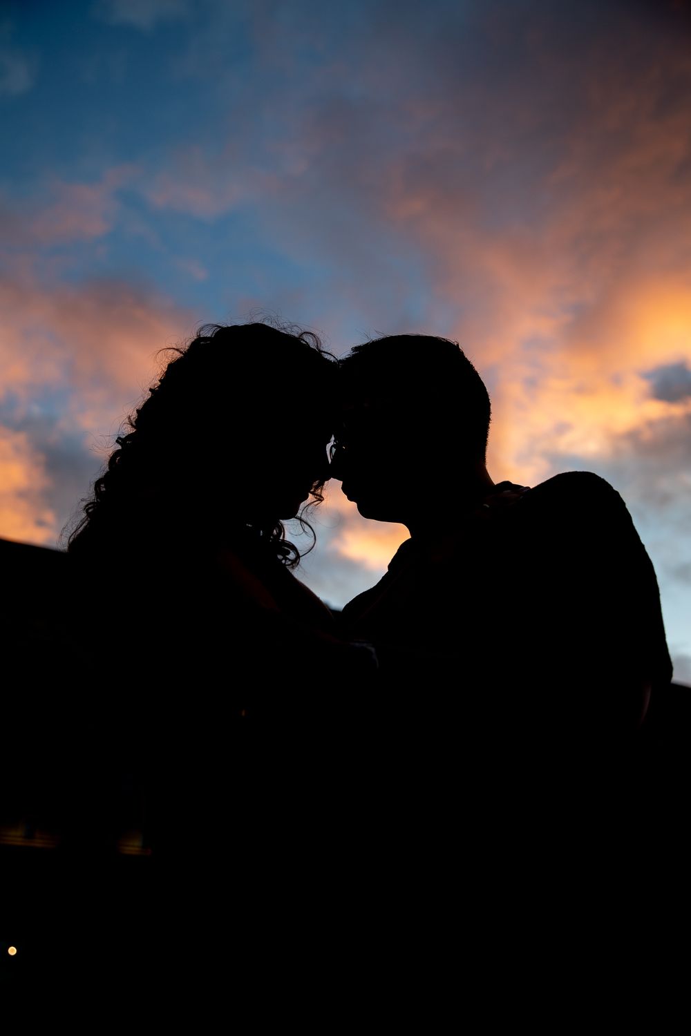 Silhouetted couple against dramatic sunset sky with orange clouds.