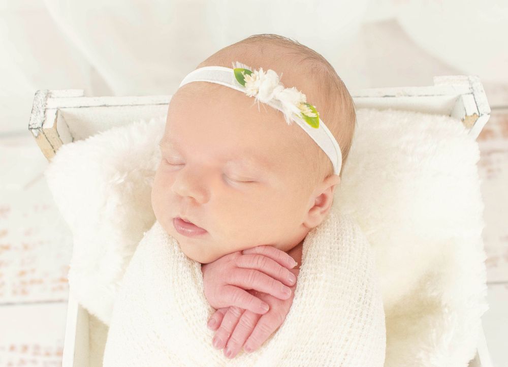 Newborn baby sleeping peacefully on white textured blanket in soft natural light.