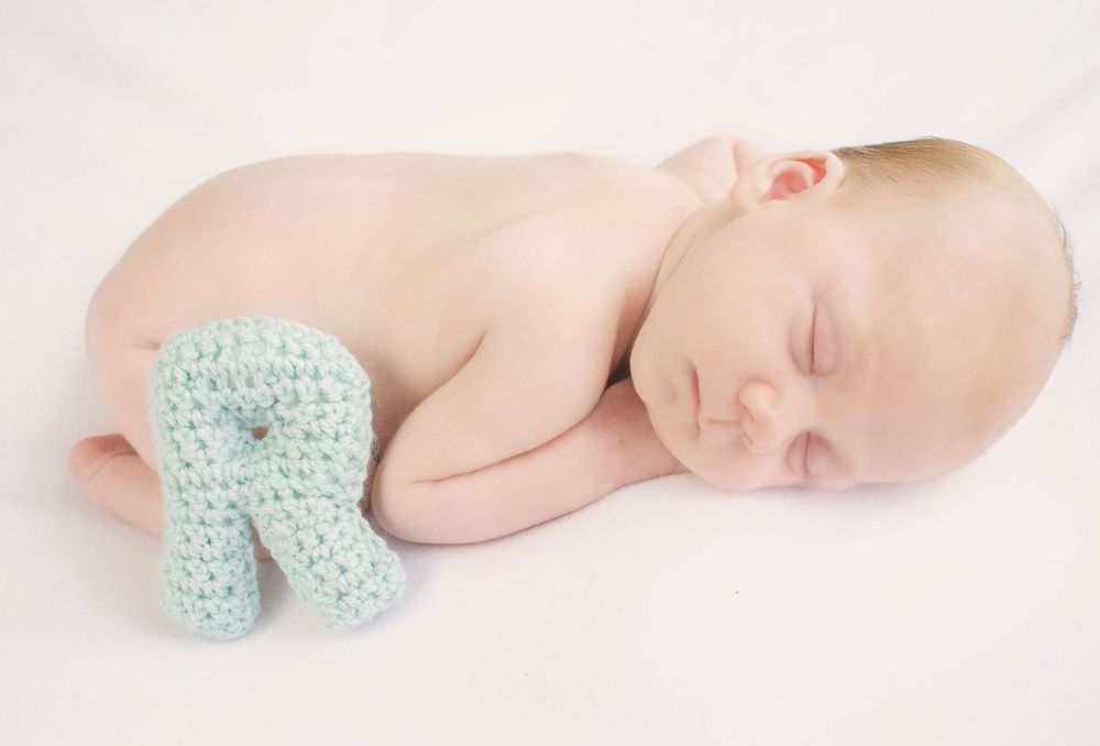 Sleeping newborn baby wearing soft mint knit outfit on white backdrop.