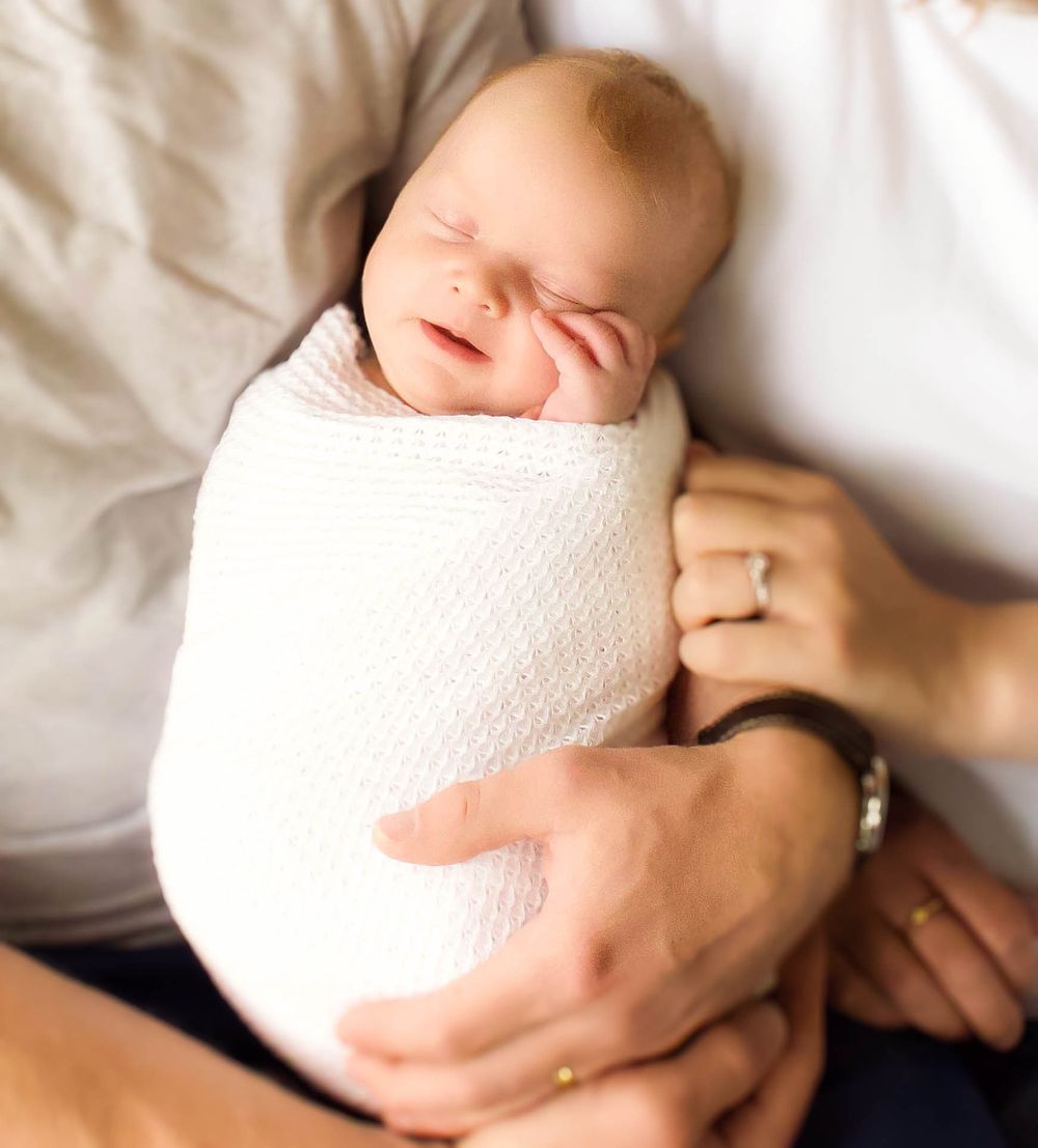 Newborn baby wrapped in white textured blanket during professional photoshoot.